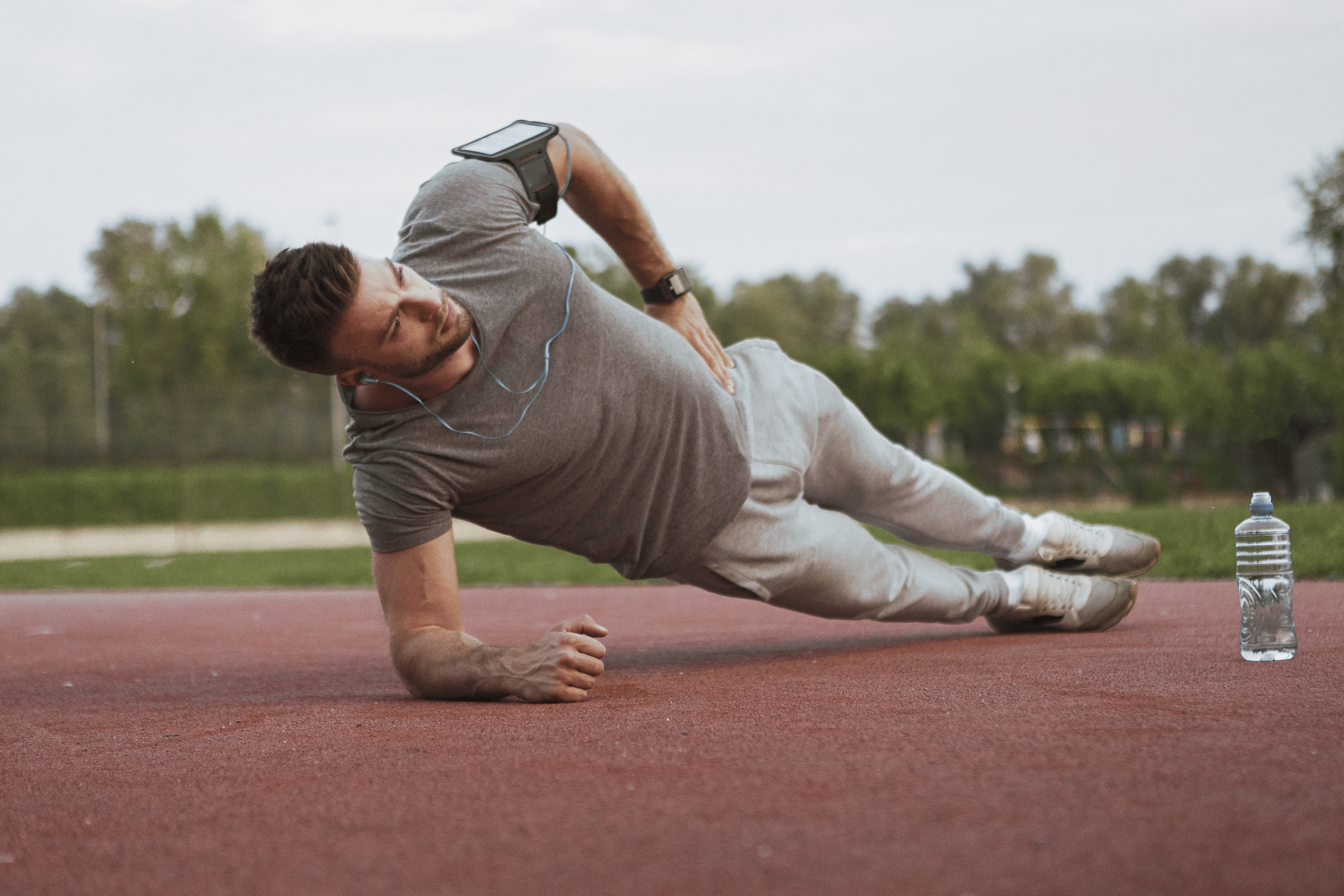 Man in gray t-shirt and sweatpants doing a side plank outside 