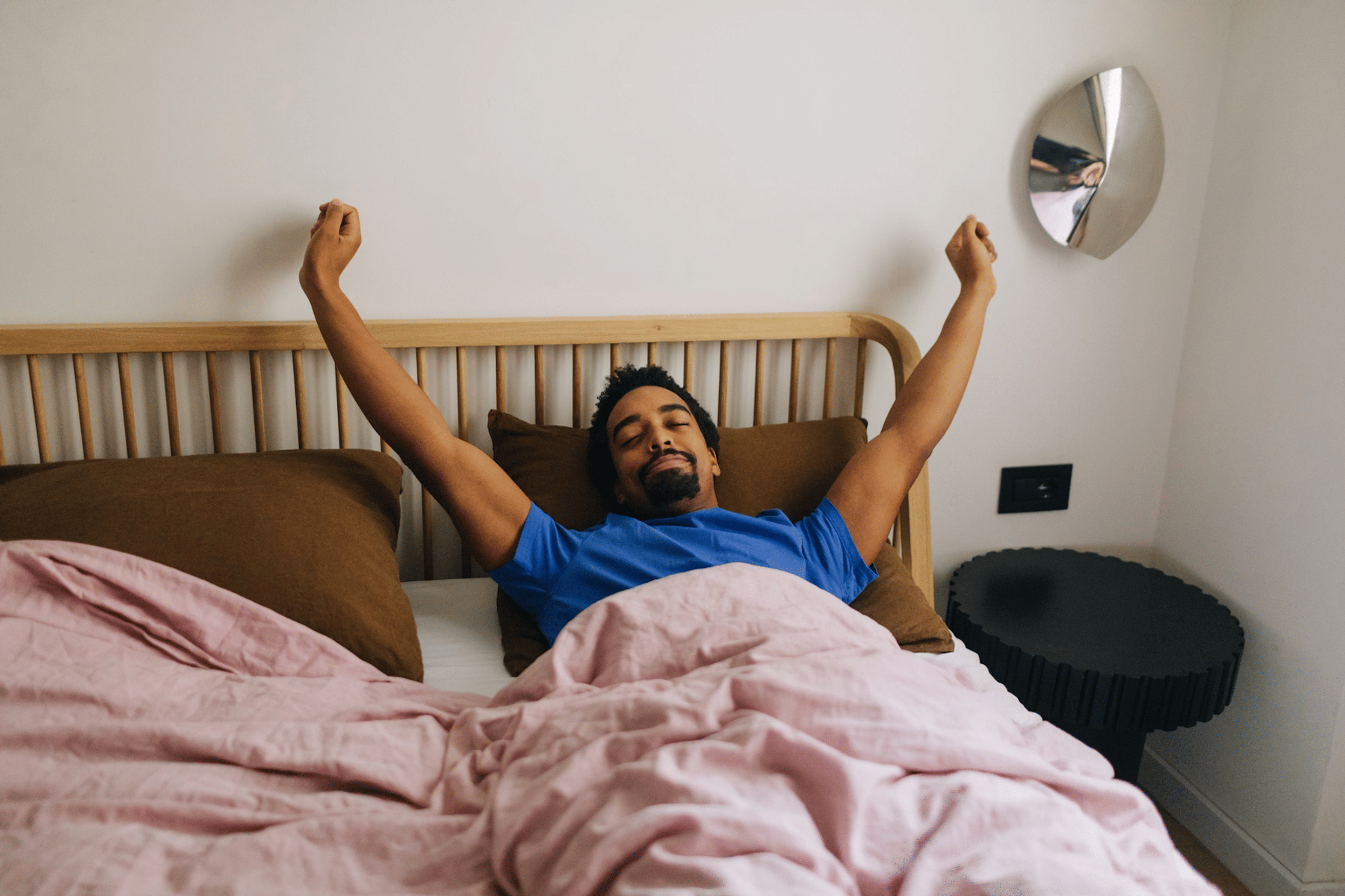 A man stretching his arms up in the air happily while lying in bed after a good night of sleep. Learn how many hours of REM sleep you need in this article.