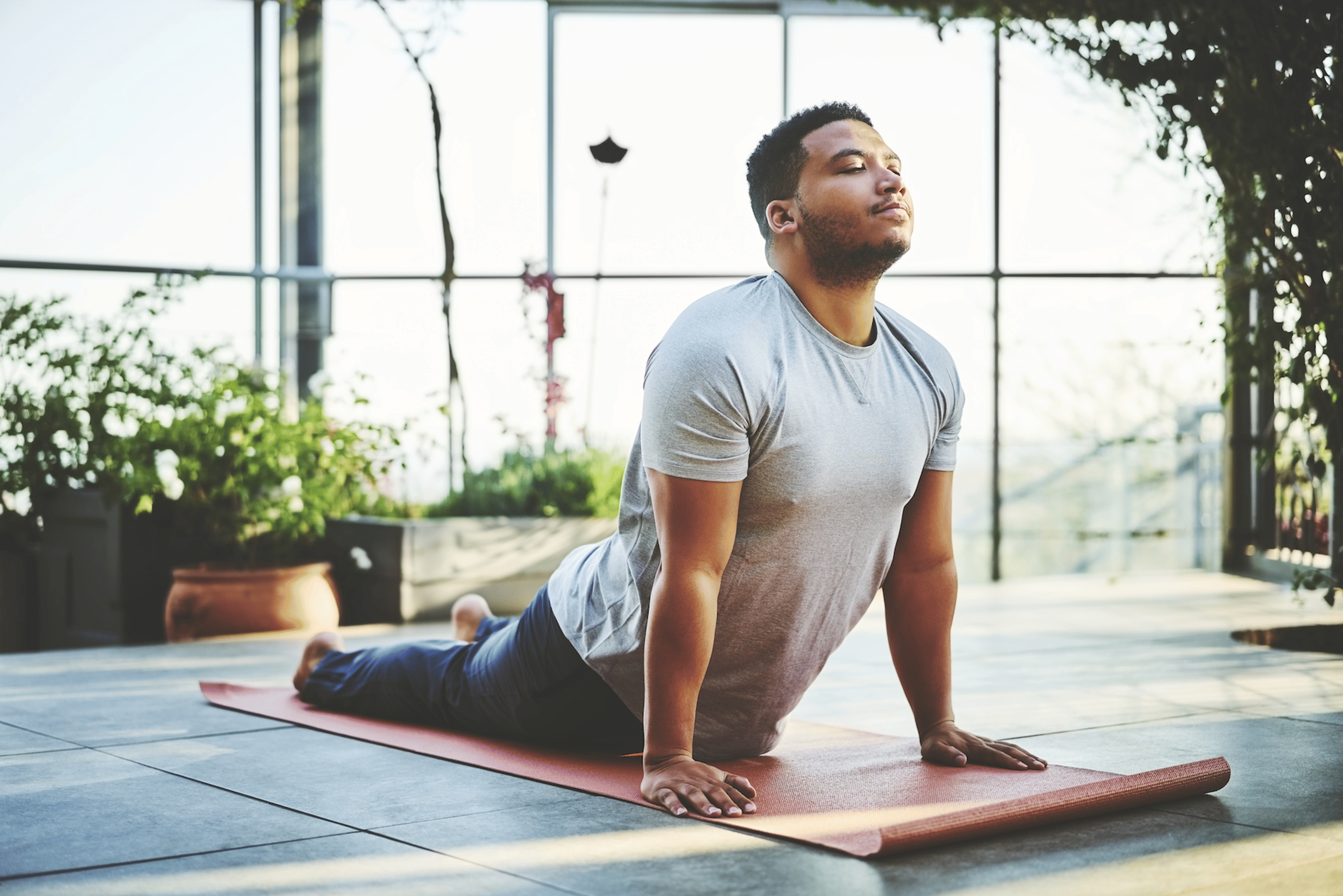 A calm man in Upward Facing Dog pose practicing yoga on his yoga mat in a sunny room at home.