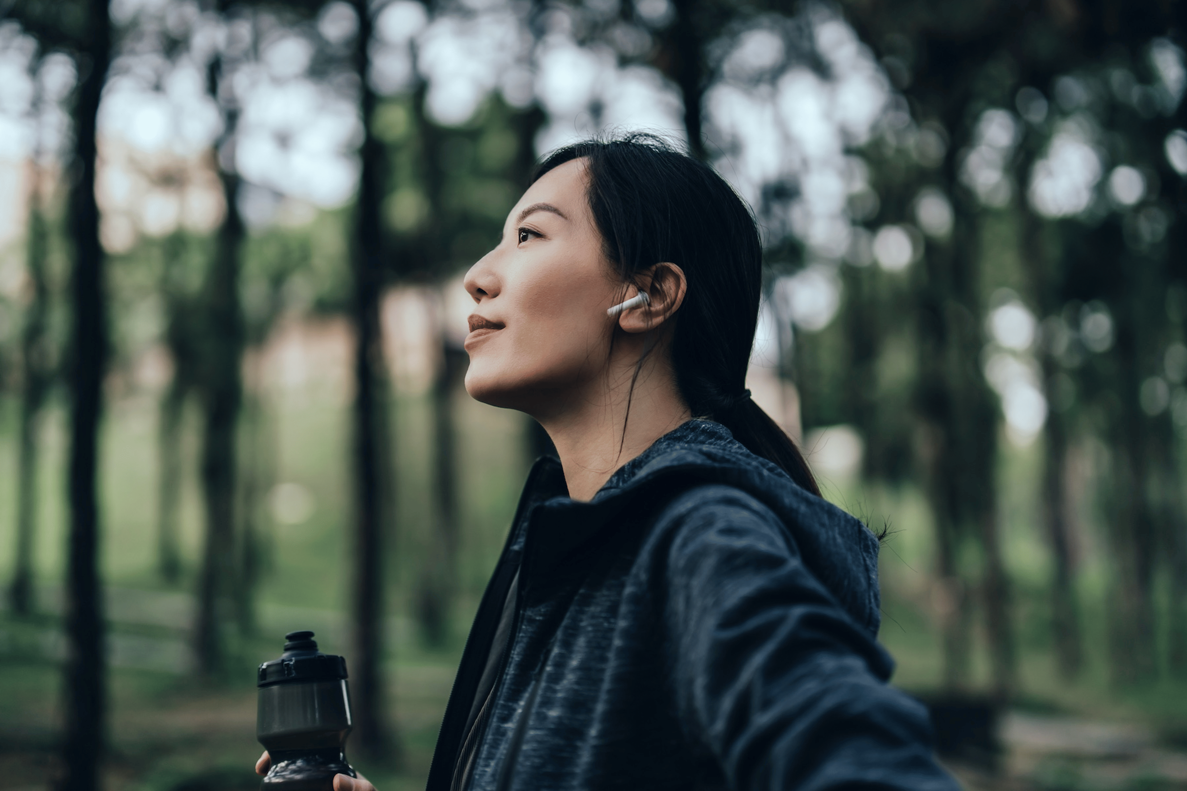A confident athlete standing in the forrest, holding a water bottle, and looking resilient. Learn how to build resilience in this article.