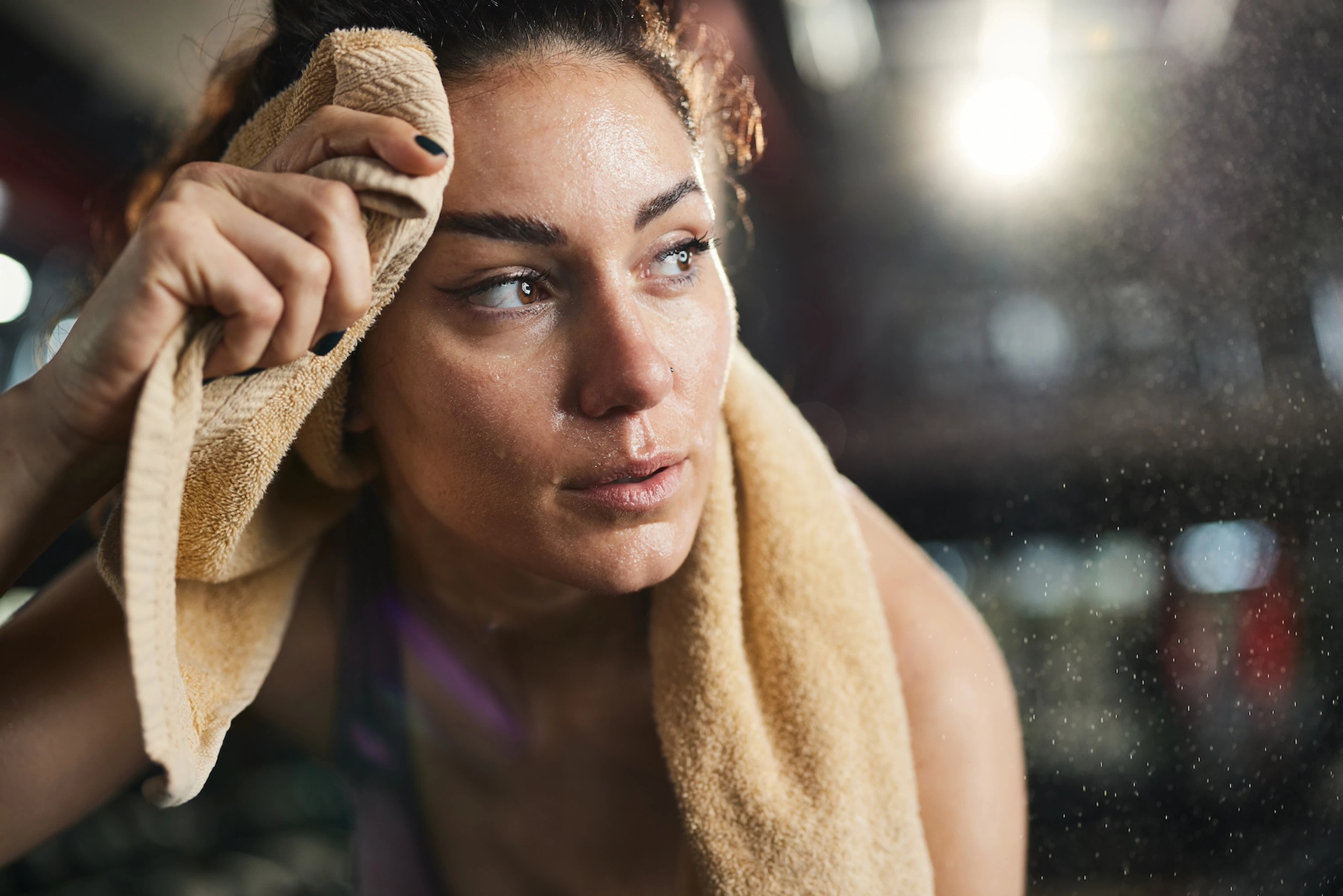 A sweaty athlete feeling lightheaded after a workout. She's resting and has a towel behind her neck and on her forehead.