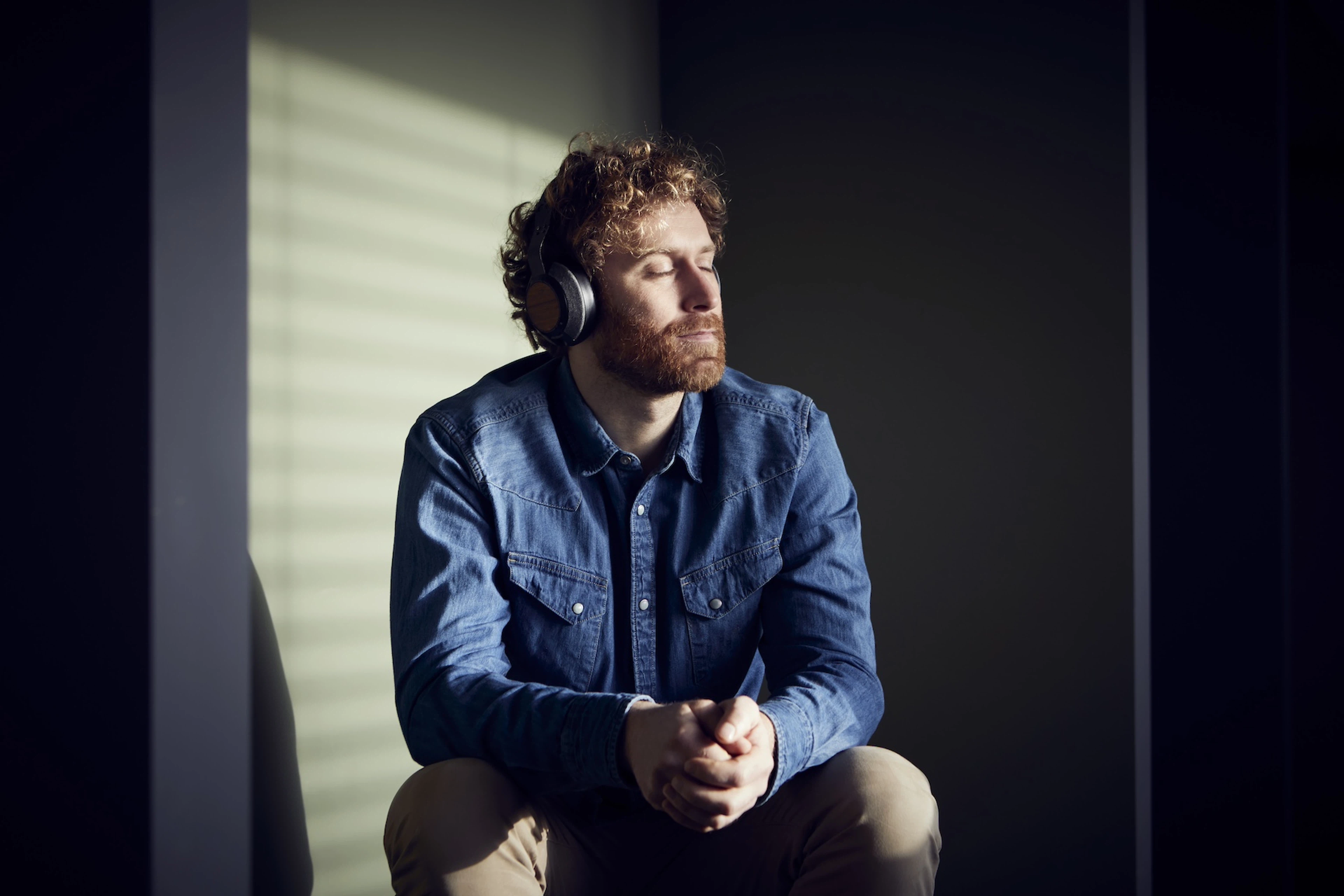 A man practicing healing meditation. He's listening to a meditation on his headphones, closing his eyes, and sitting down.