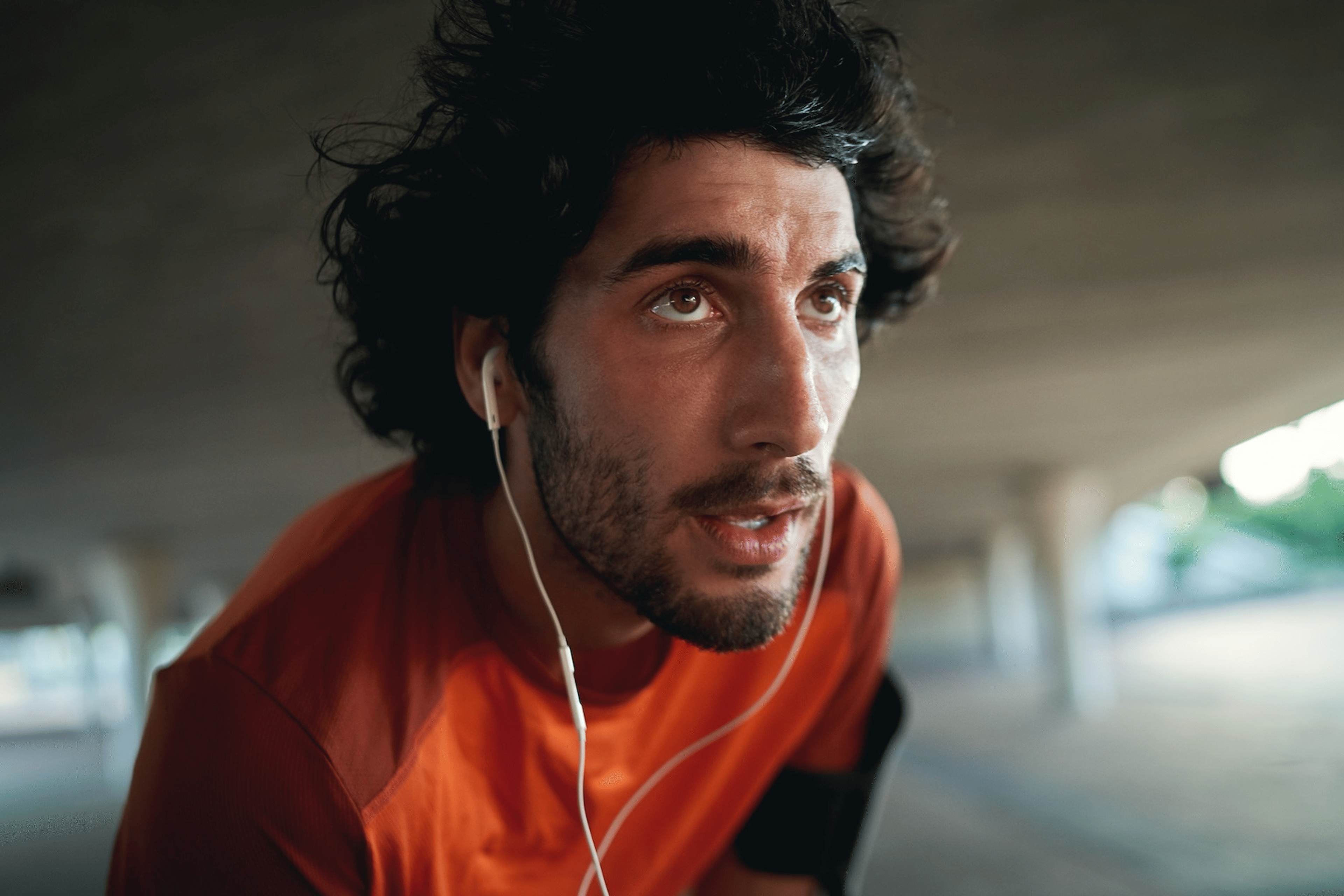 A close-up photo of a sweaty young man listening to headphones who just finished his workout.