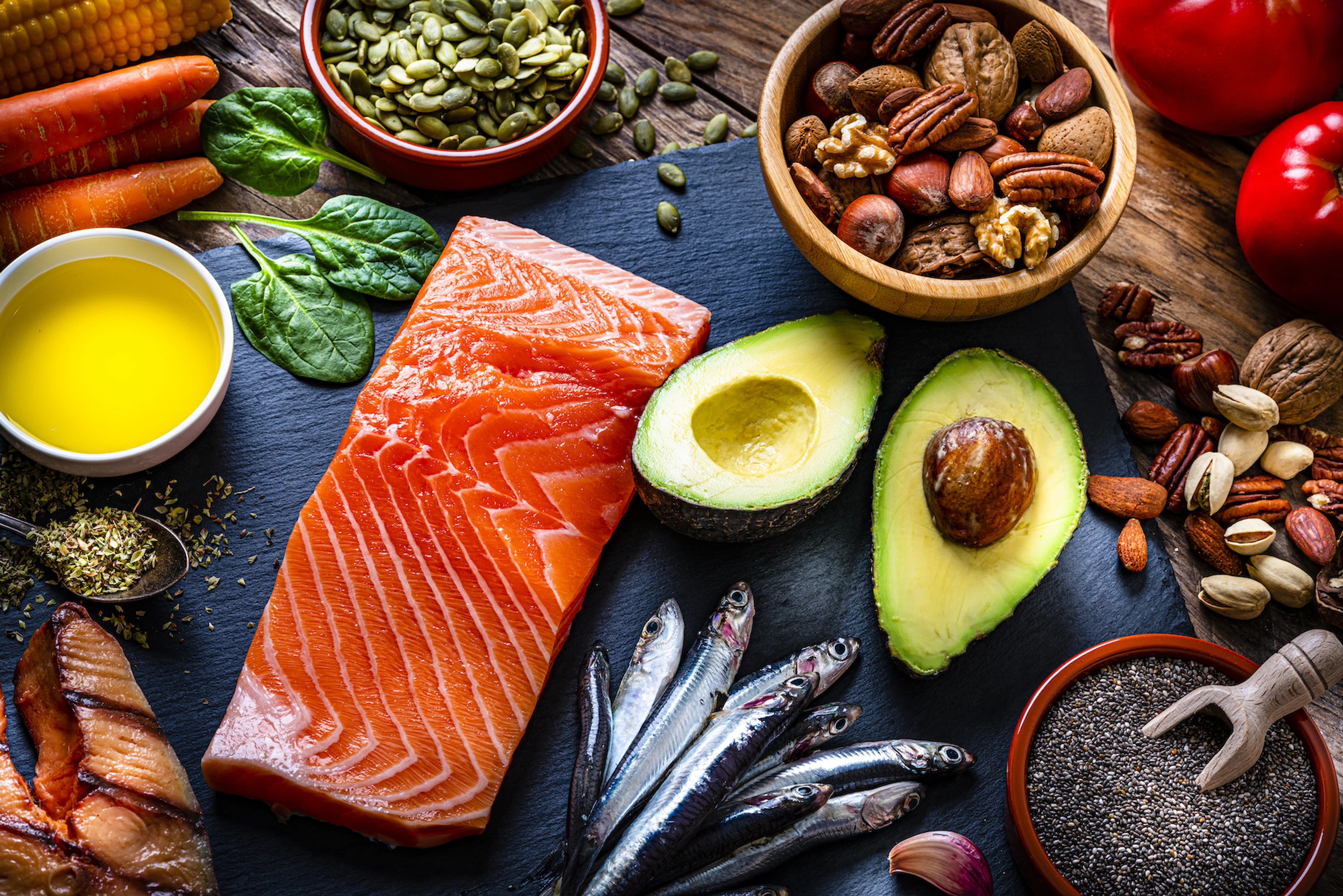 A flay-lay image of foods with healthy fats, like fish, avocados, and nuts.