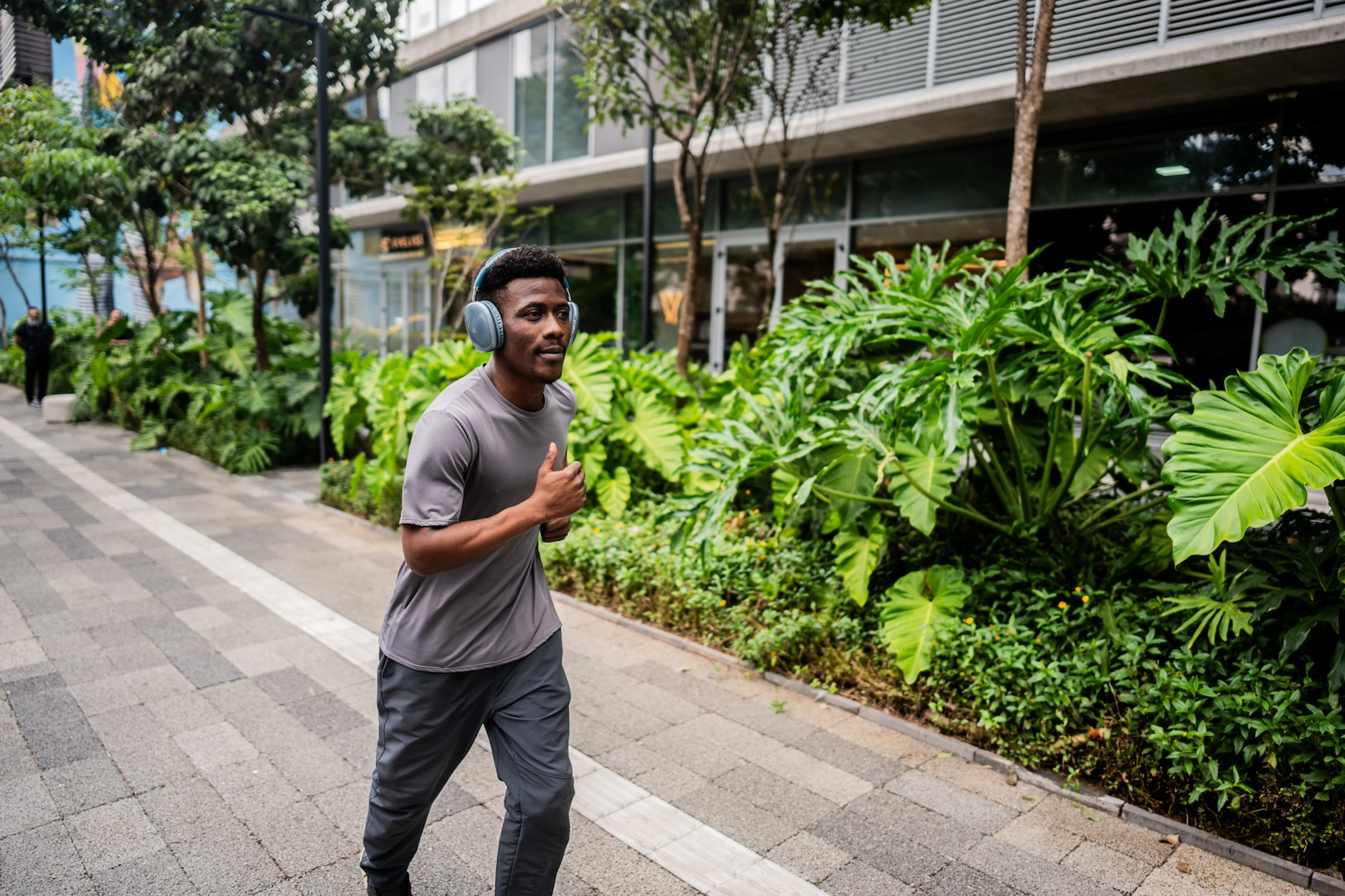 A young man running outside on a city sidewalk while wearing headphones.