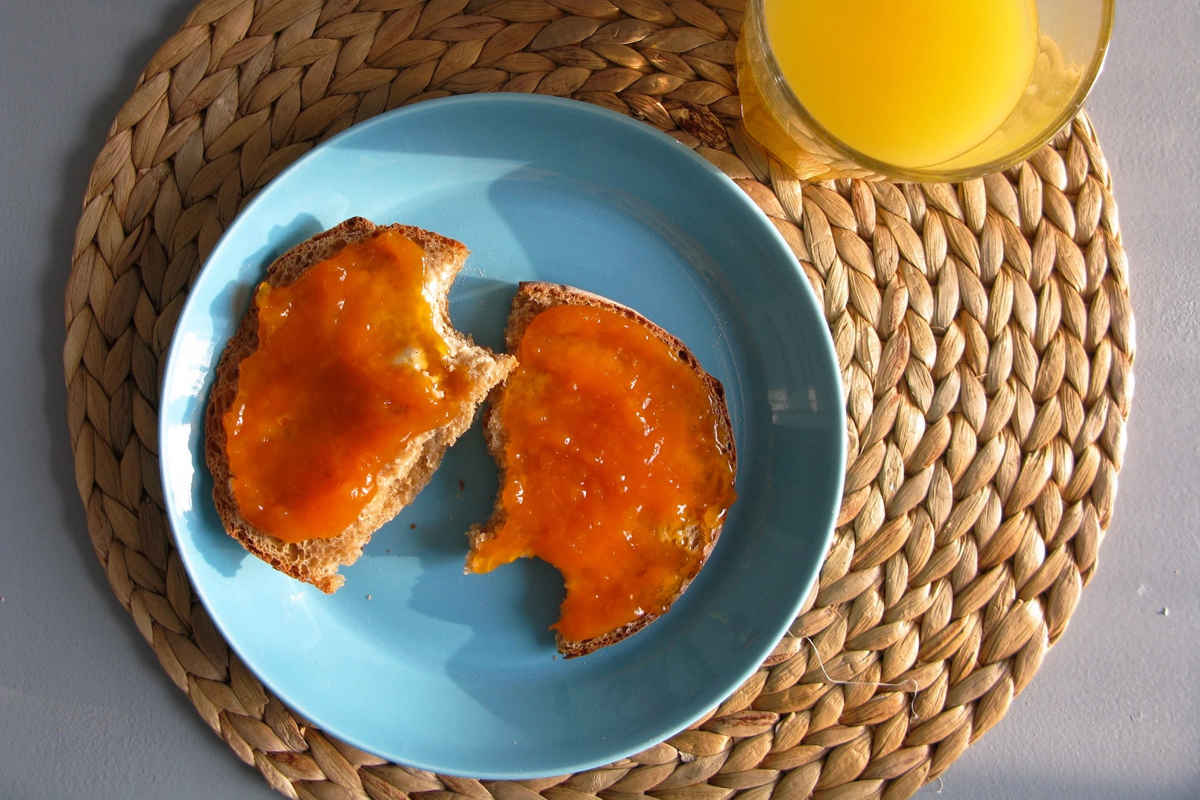 An English muffin cut in half with jam on a blue plate next to a glass of orange juice.