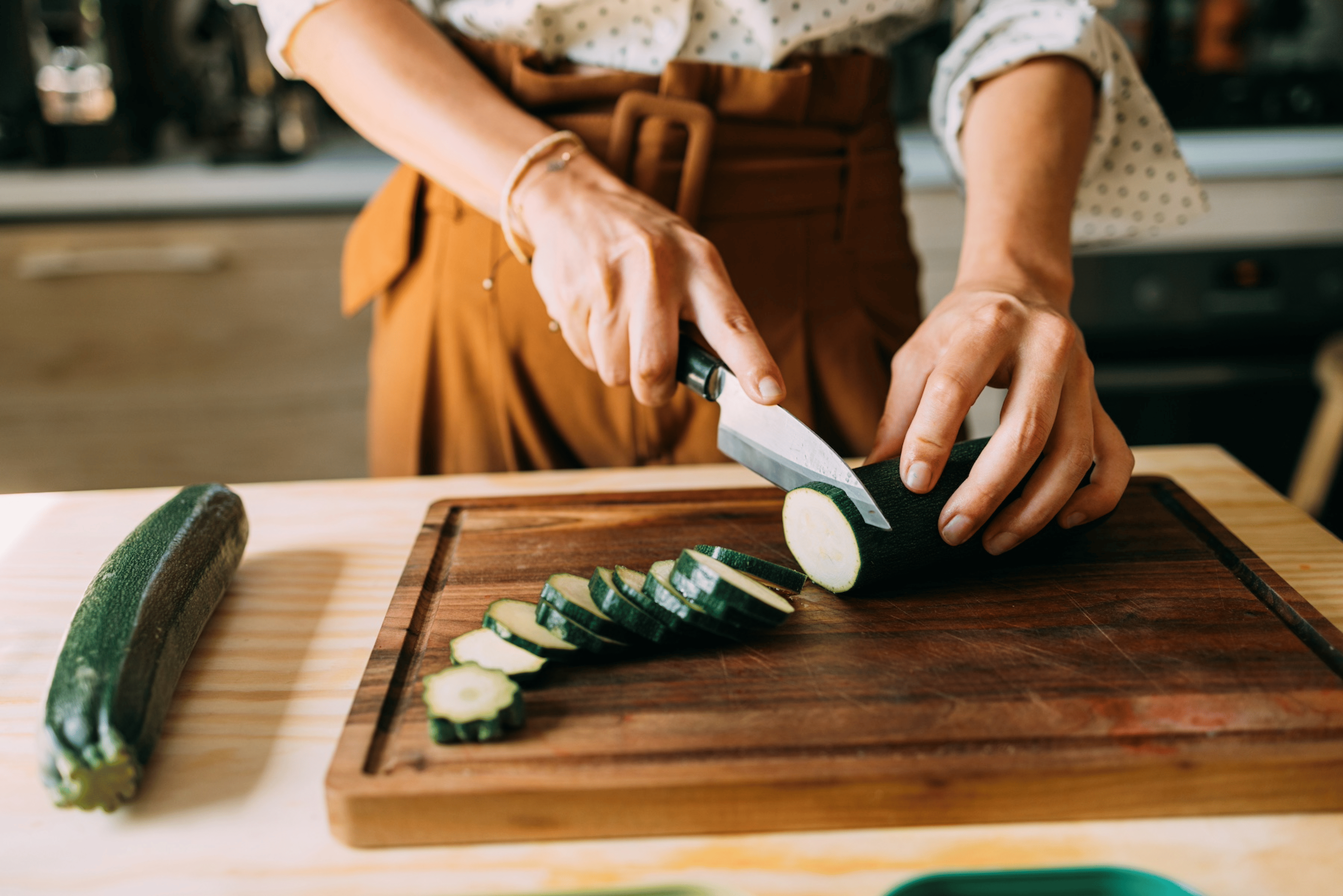 A person chopping a zucchini, a hydrating food, into slices.