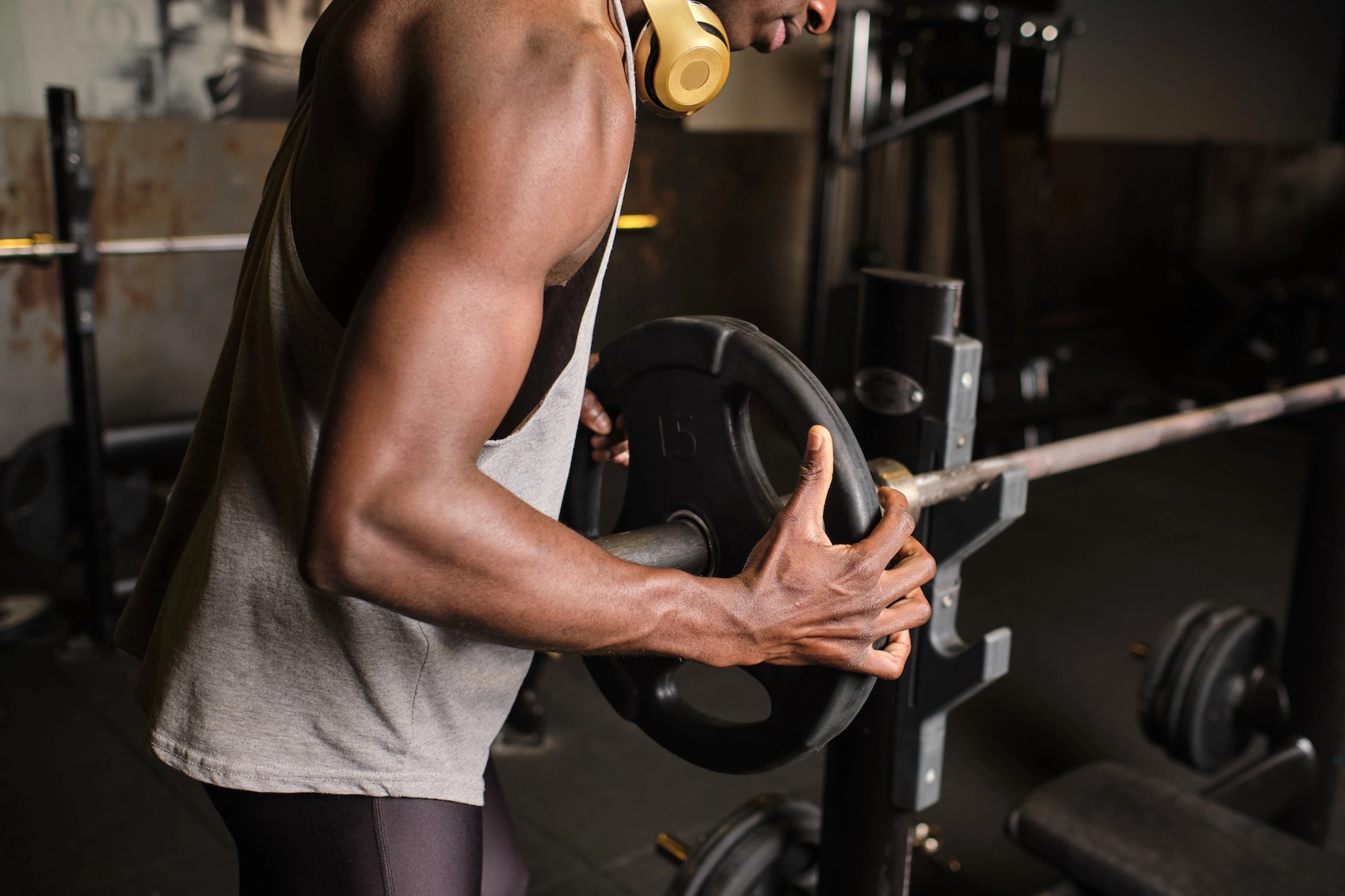 A close-up photo of a man loading a plate onto a barbell at the gym.