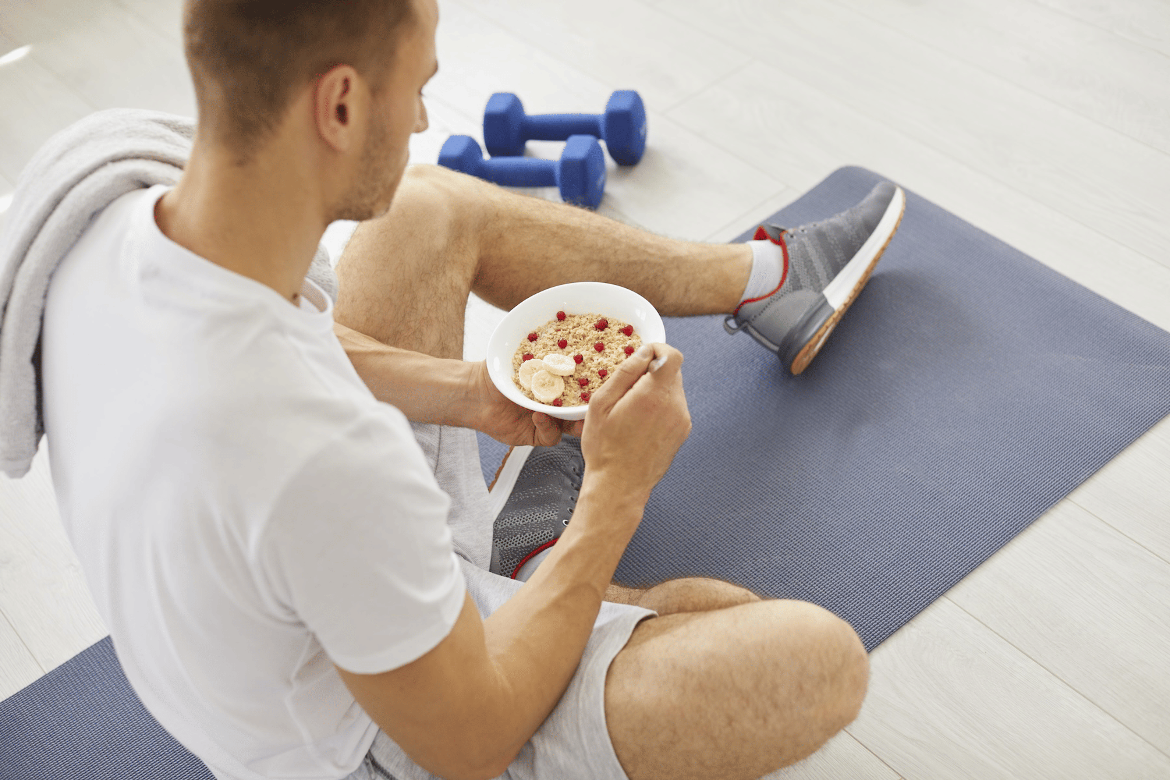 A man eating oatmeal and fruit with an optimal carb-to-protein ratio on a yoga mat after finishing a workout.