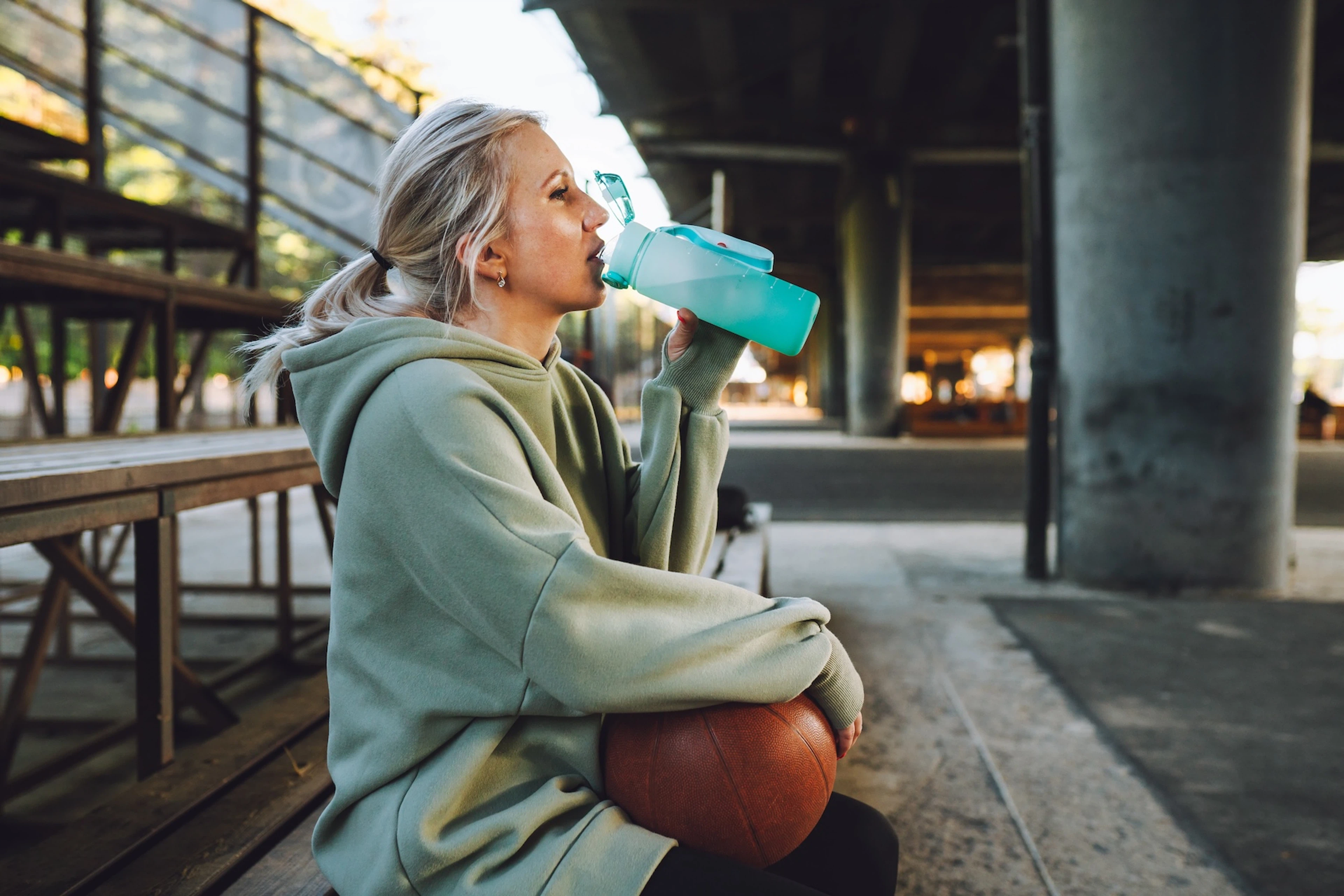 A woman drinking an electrolyte drink after an outdoor basketball game.