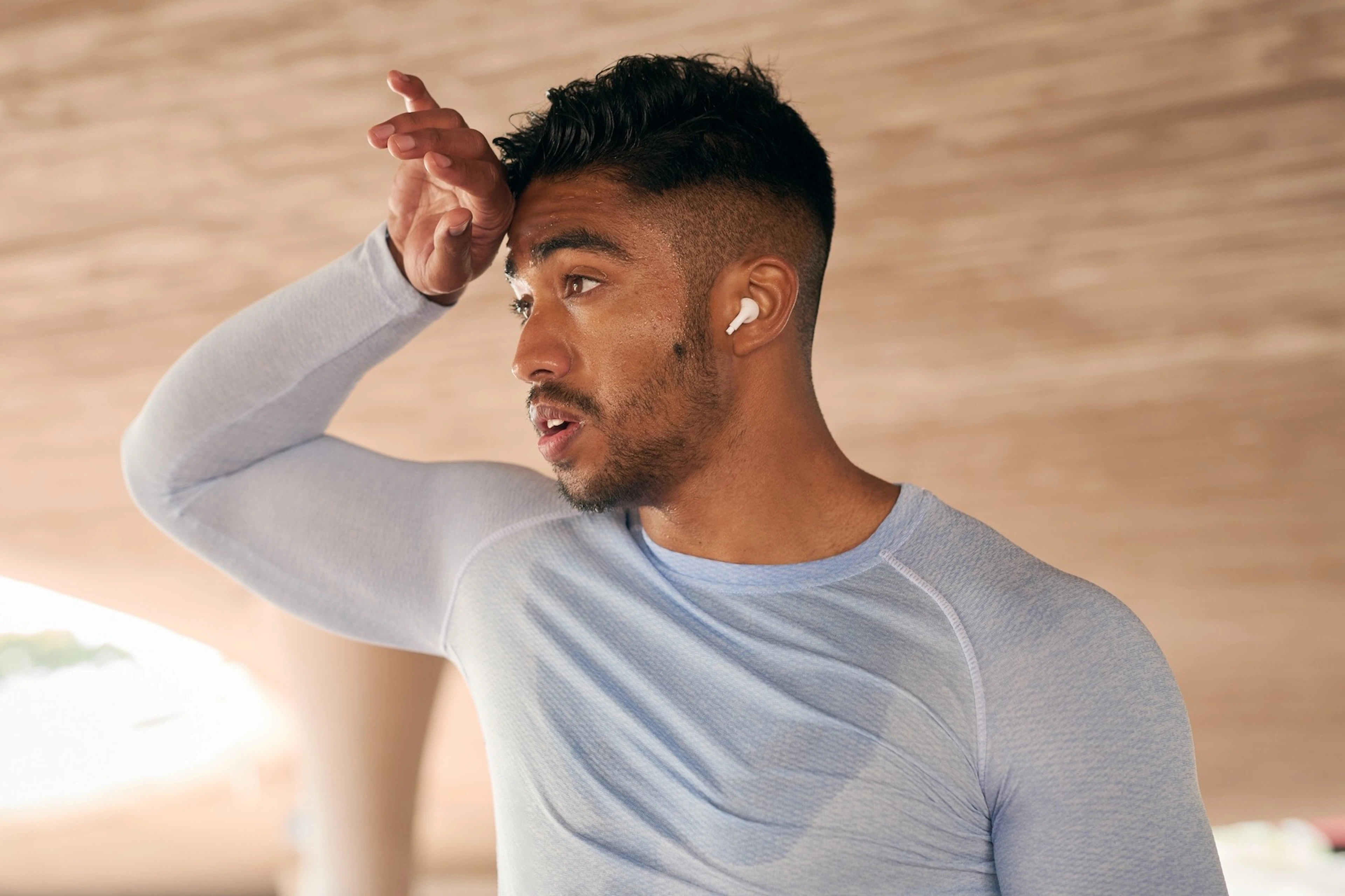 A man exercising in the heat, wiping his sweat from his forehood.