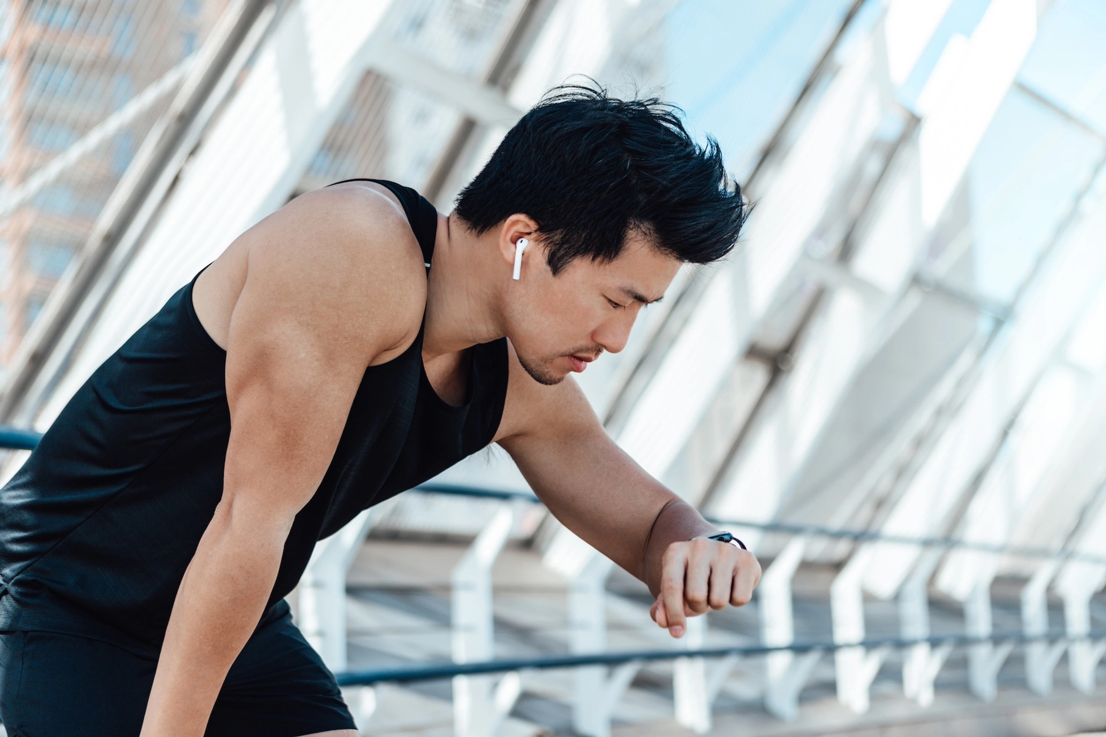 A man looking at his fitness watch after exercising and resting his hand on his knee. He is experiencing signs of overtraining like a decline in performance and fatigue.