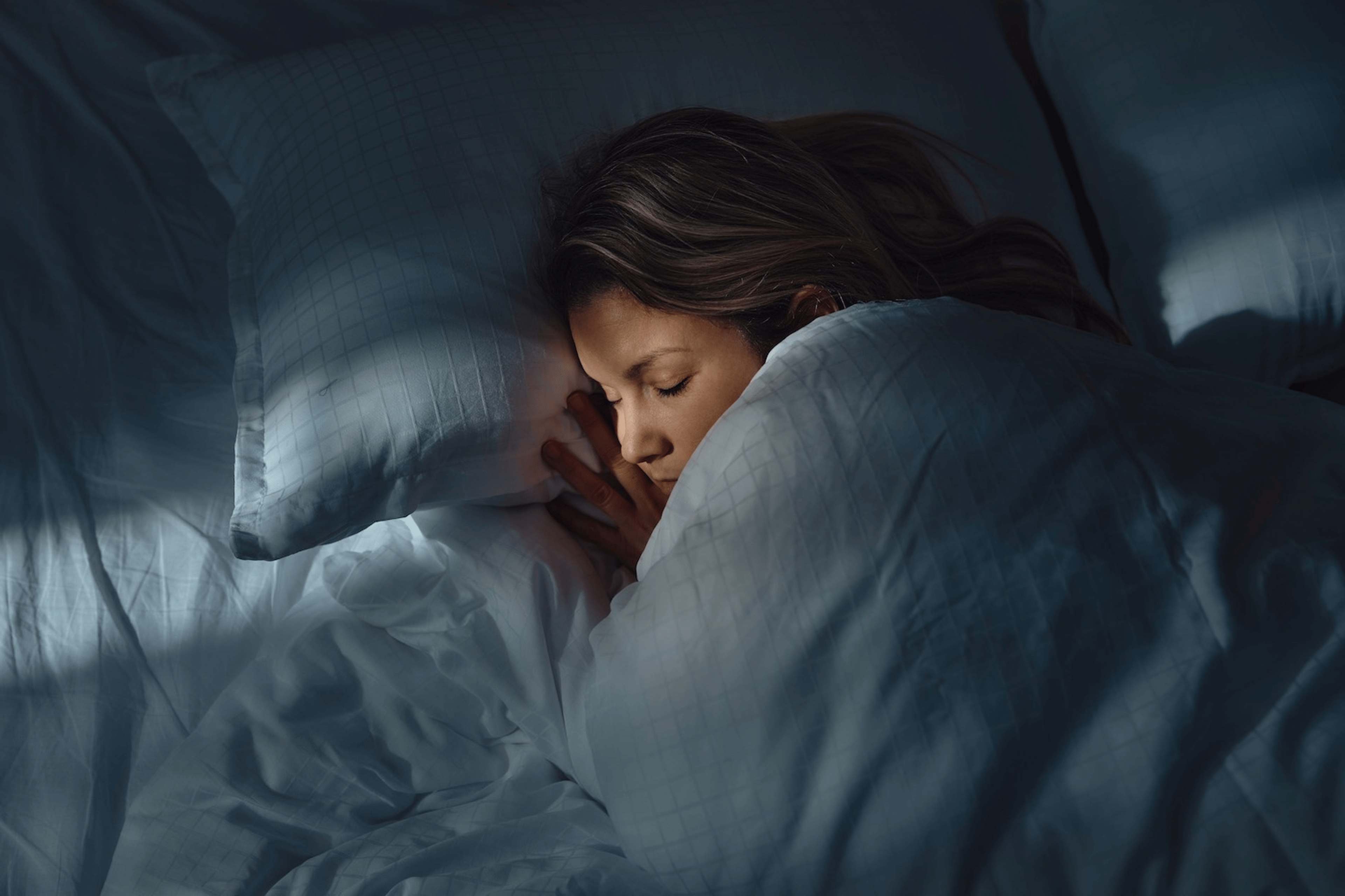 A woman spending time in deep sleep. She's asleep under the covers in a dark bedroom.