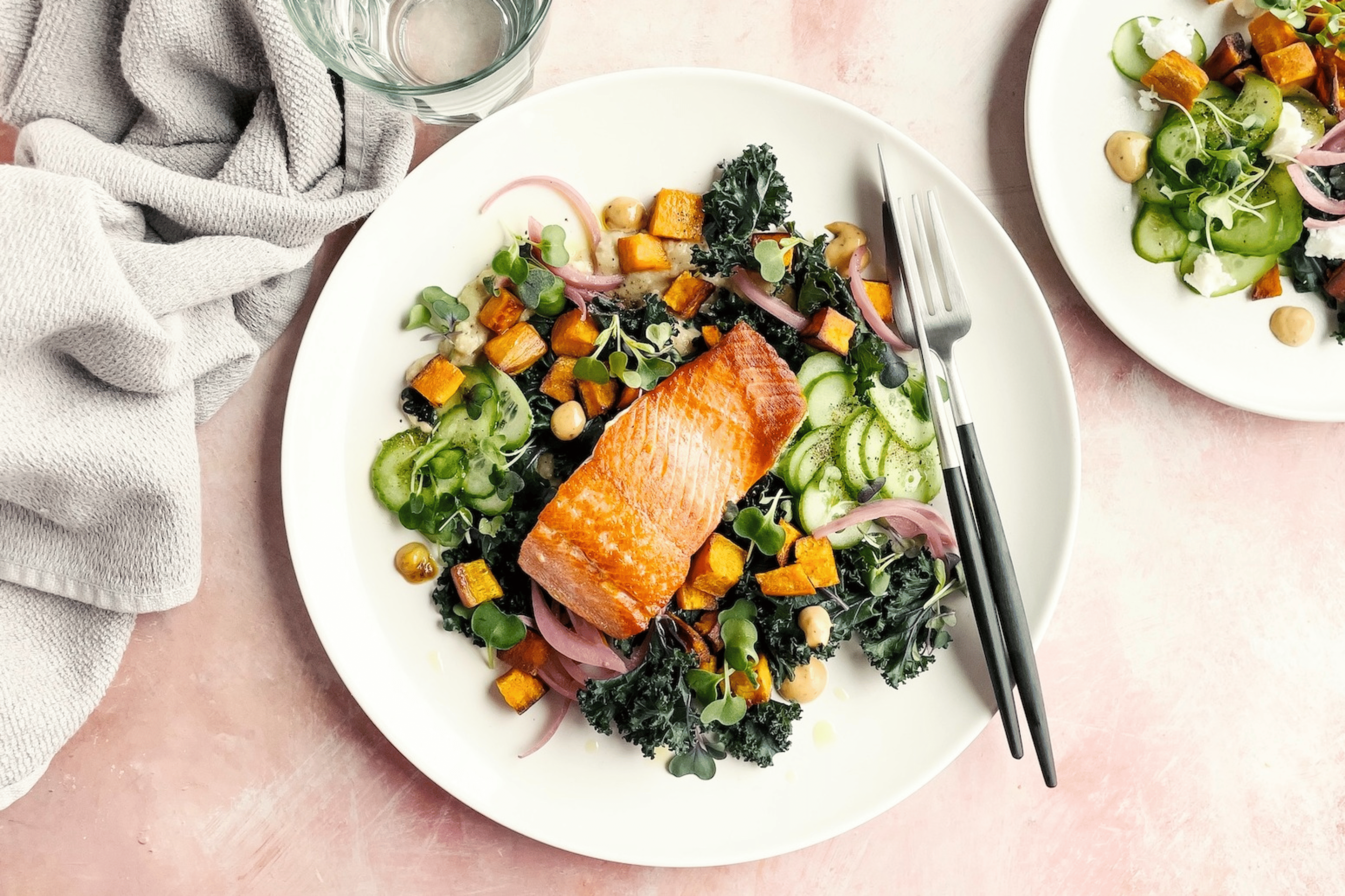 A plate of salmon (a creatine-rich food) atop a kale salad on a light pink background.