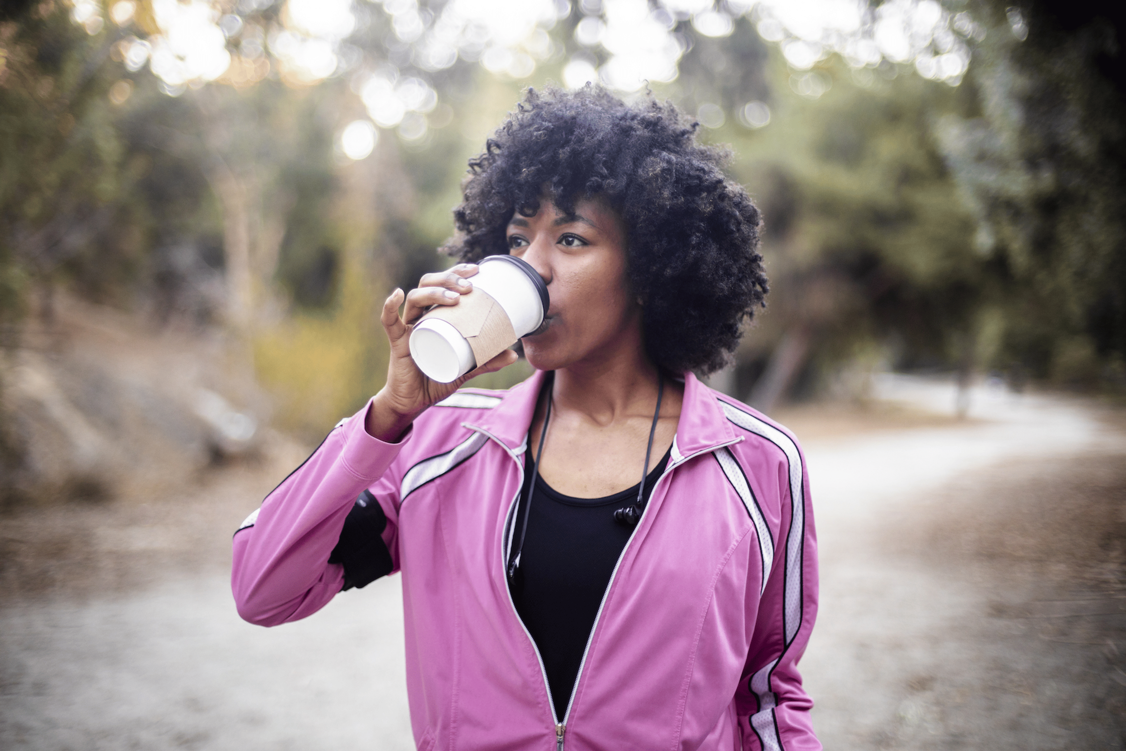 A young woman going for a walk outdoors in workout gear while drinking coffee before a workout.