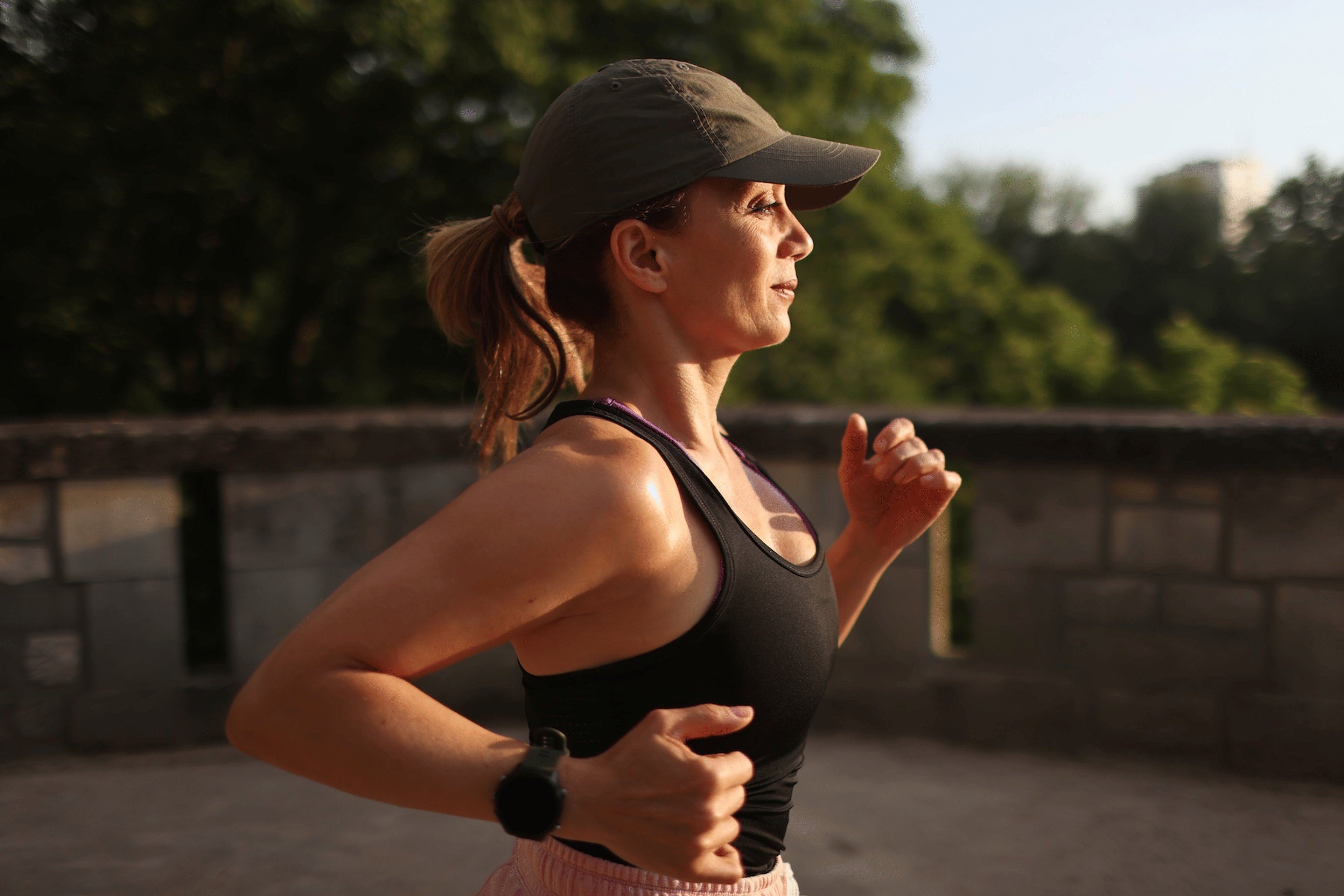 A side-profile photo of a woman going for an outdoor run in a tank top and hat.