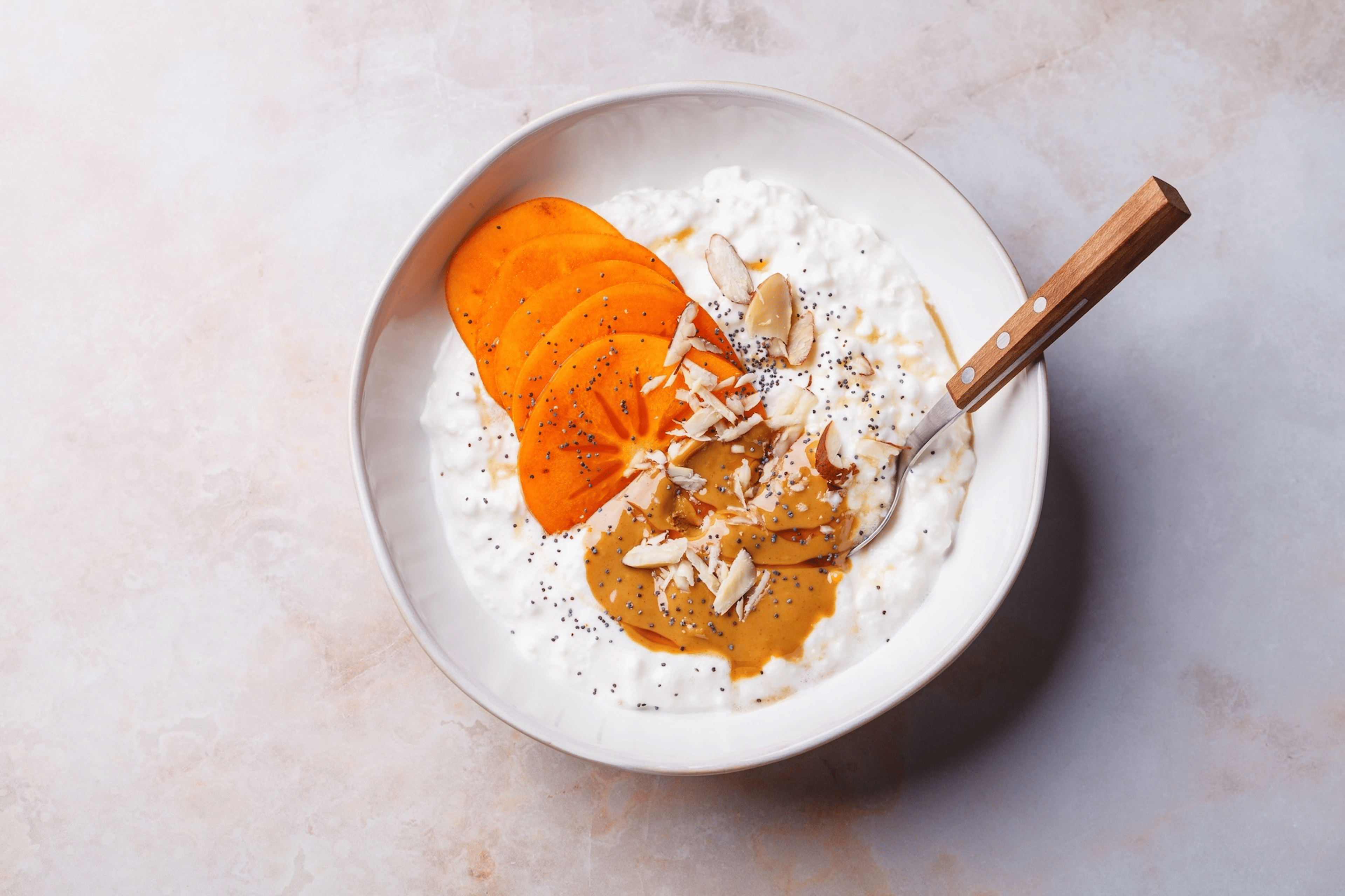 A bowl of cottage cheese with peanut butter, persimmon, and nuts.