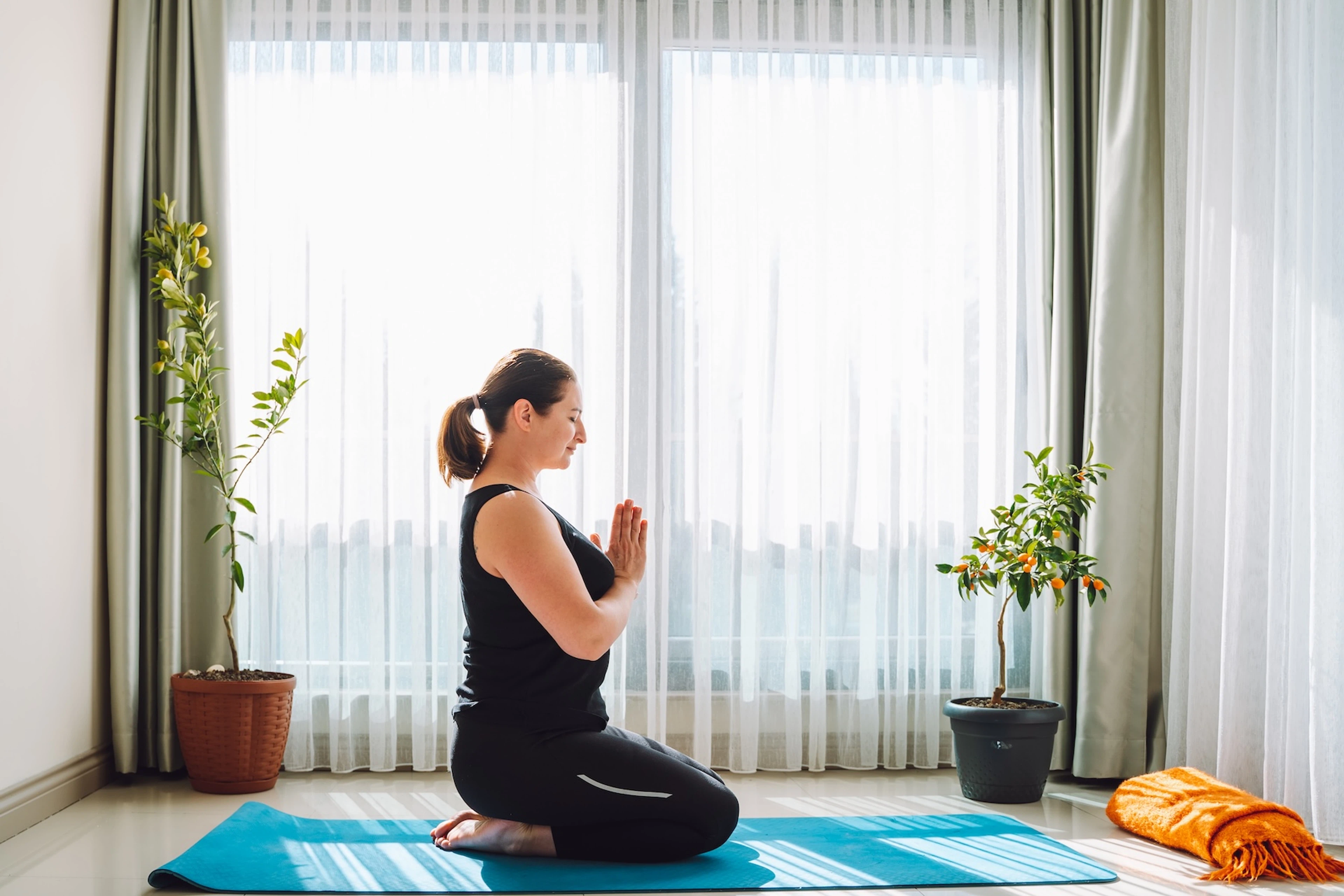 A woman in Hero Pose with prayer hands. She is practicing yoga at home to improve her mindset.