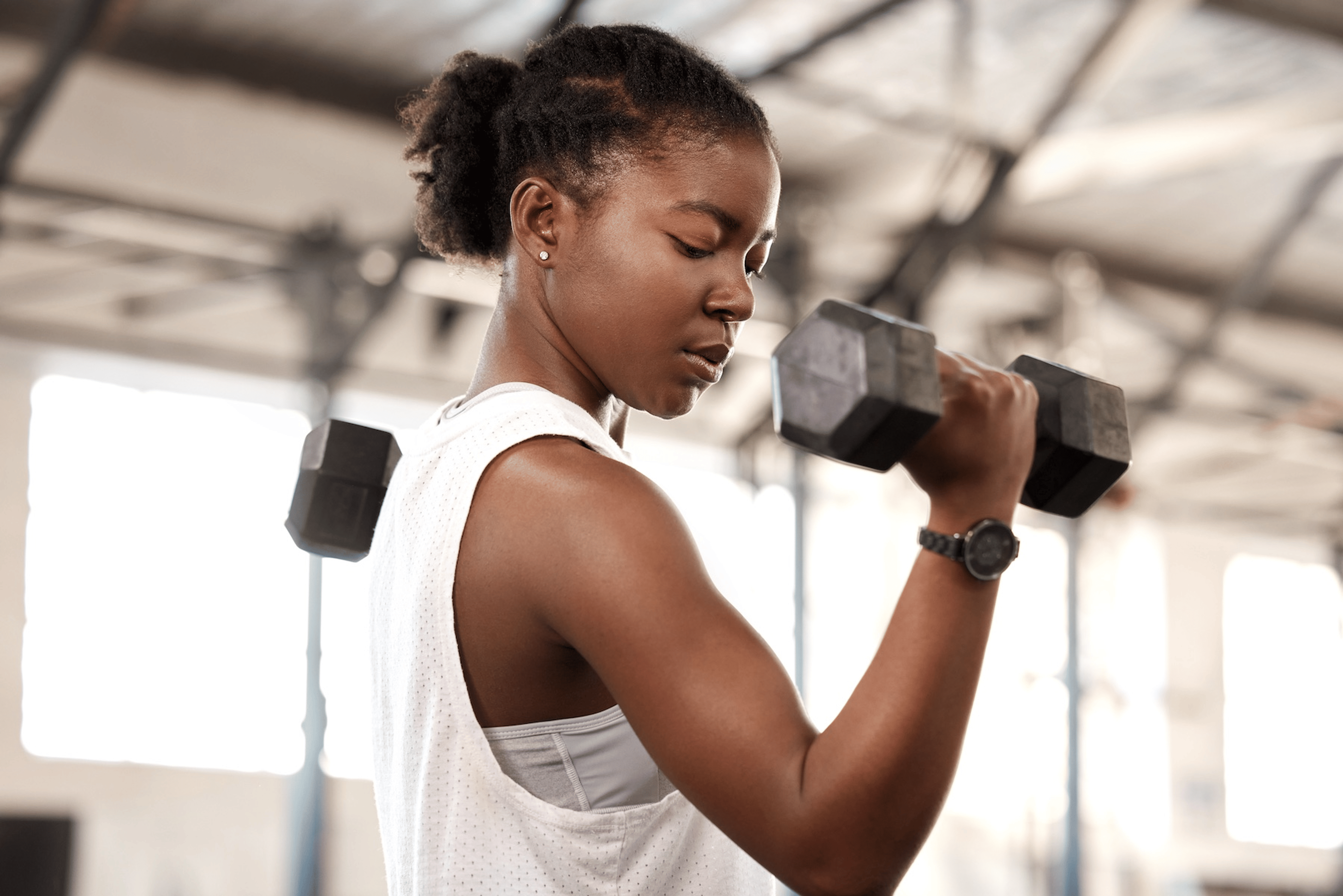 A woman in a gym doing an arm strength training workout with dumbbells.