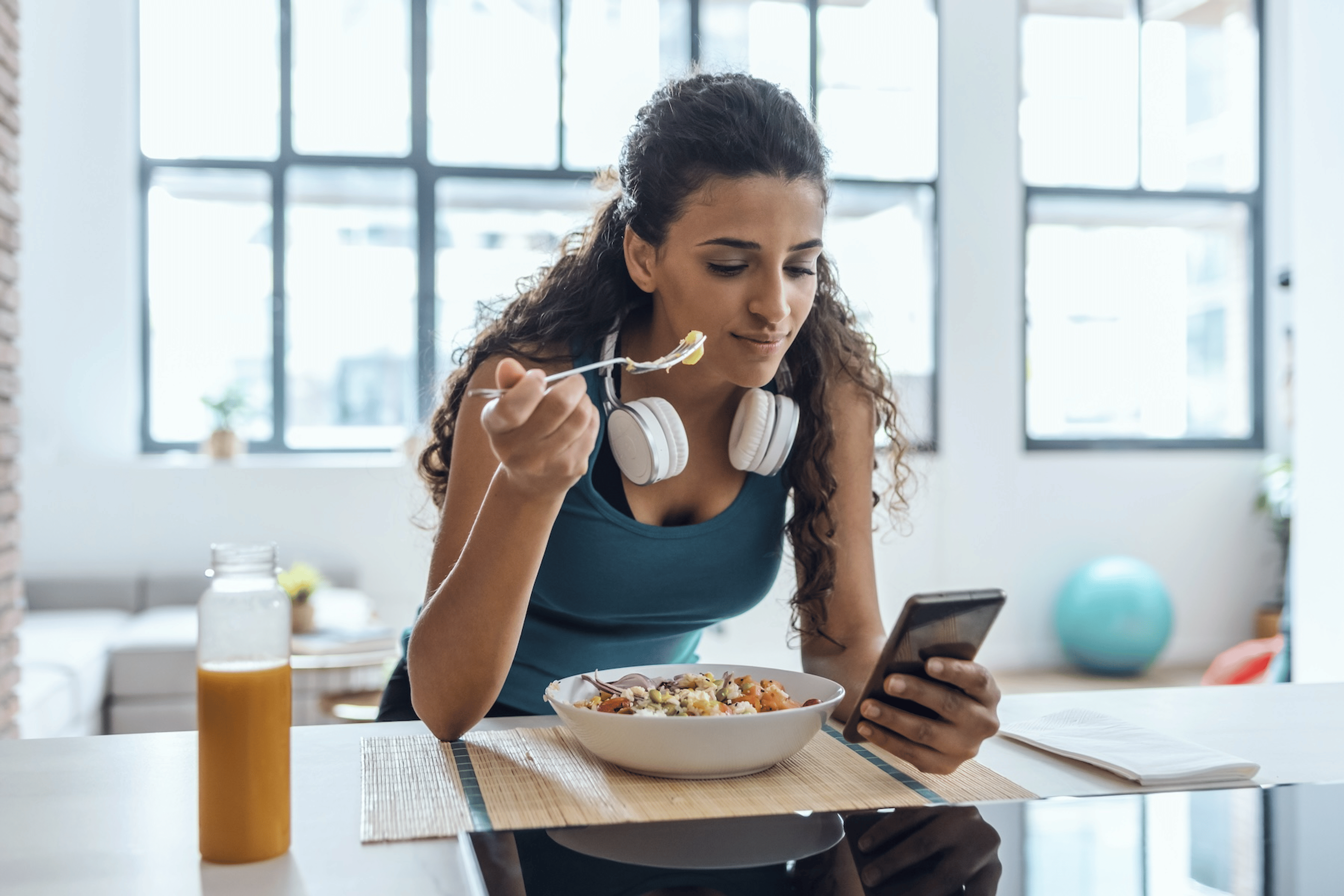 A woman eating after a workout and looking at her phone.