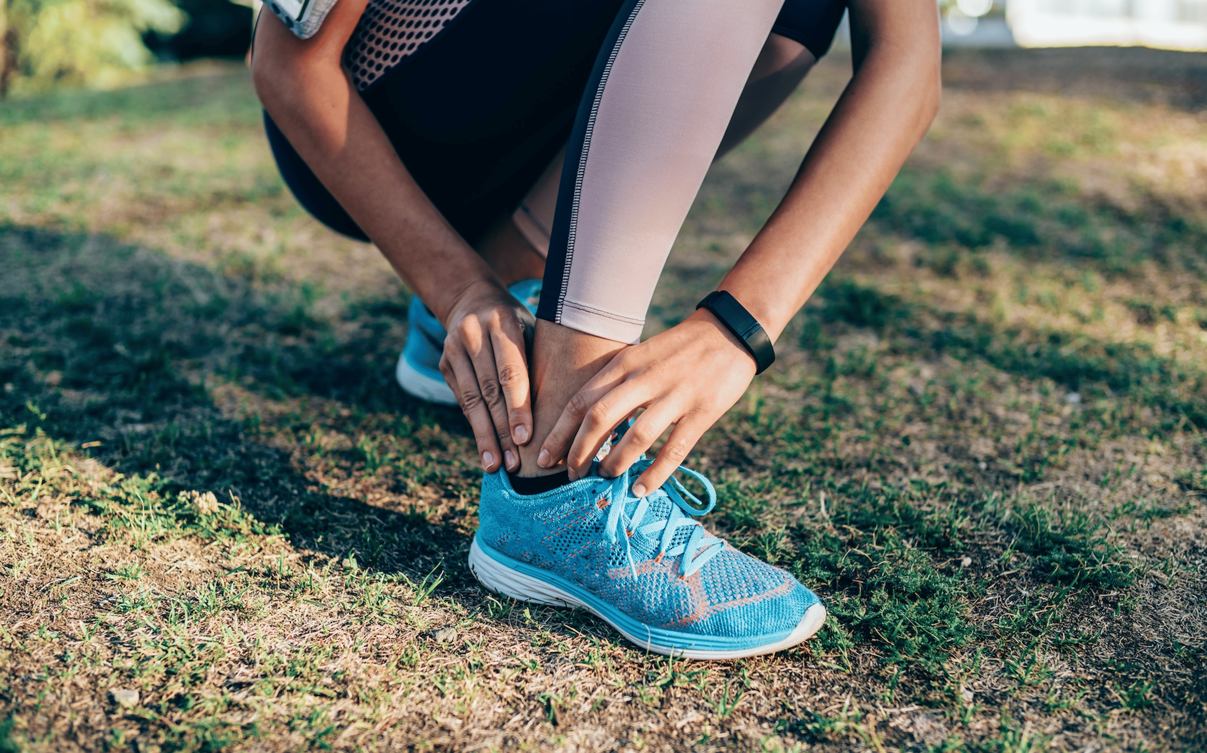 A close-up photo of an athlete resting their hands on their ankle. They're experiencing ankle pain after running.