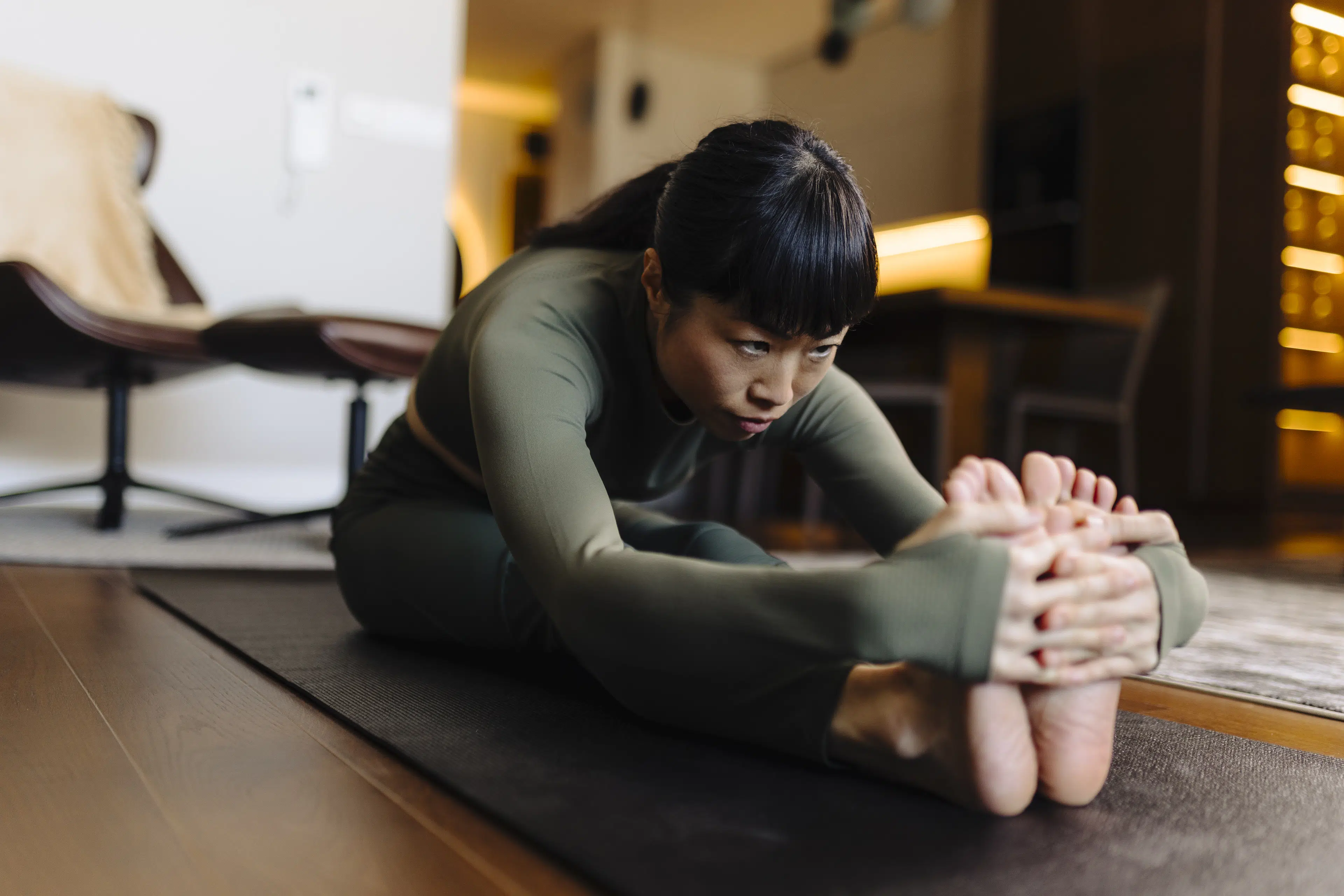 Woman doing a Seated Forward Fold in her living room at home during a practice of seated yoga poses