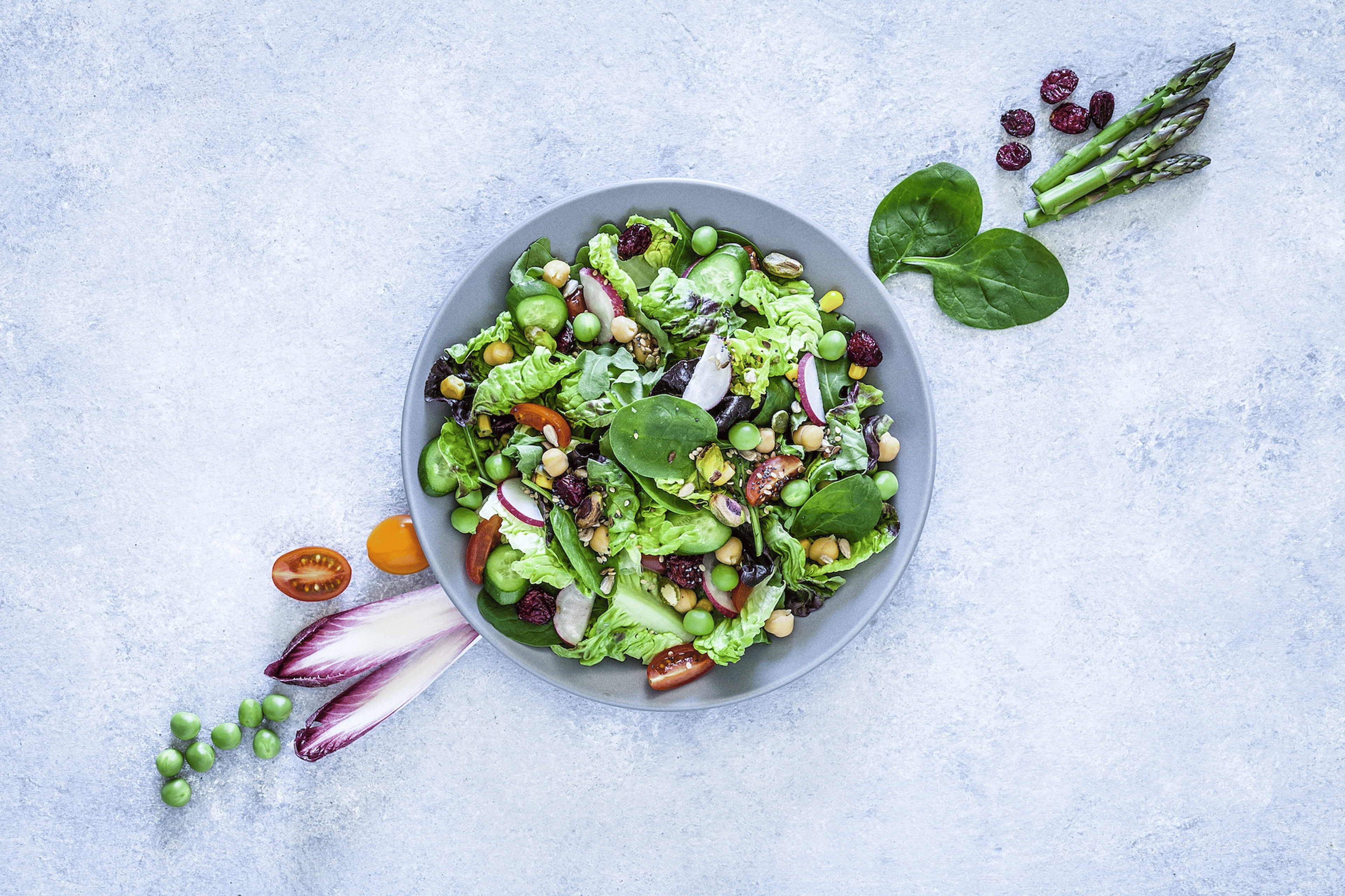 A flat-lay photo of a green salad on a neutral countertop. The salad includes high-protein vegetables including green peas and spinach.