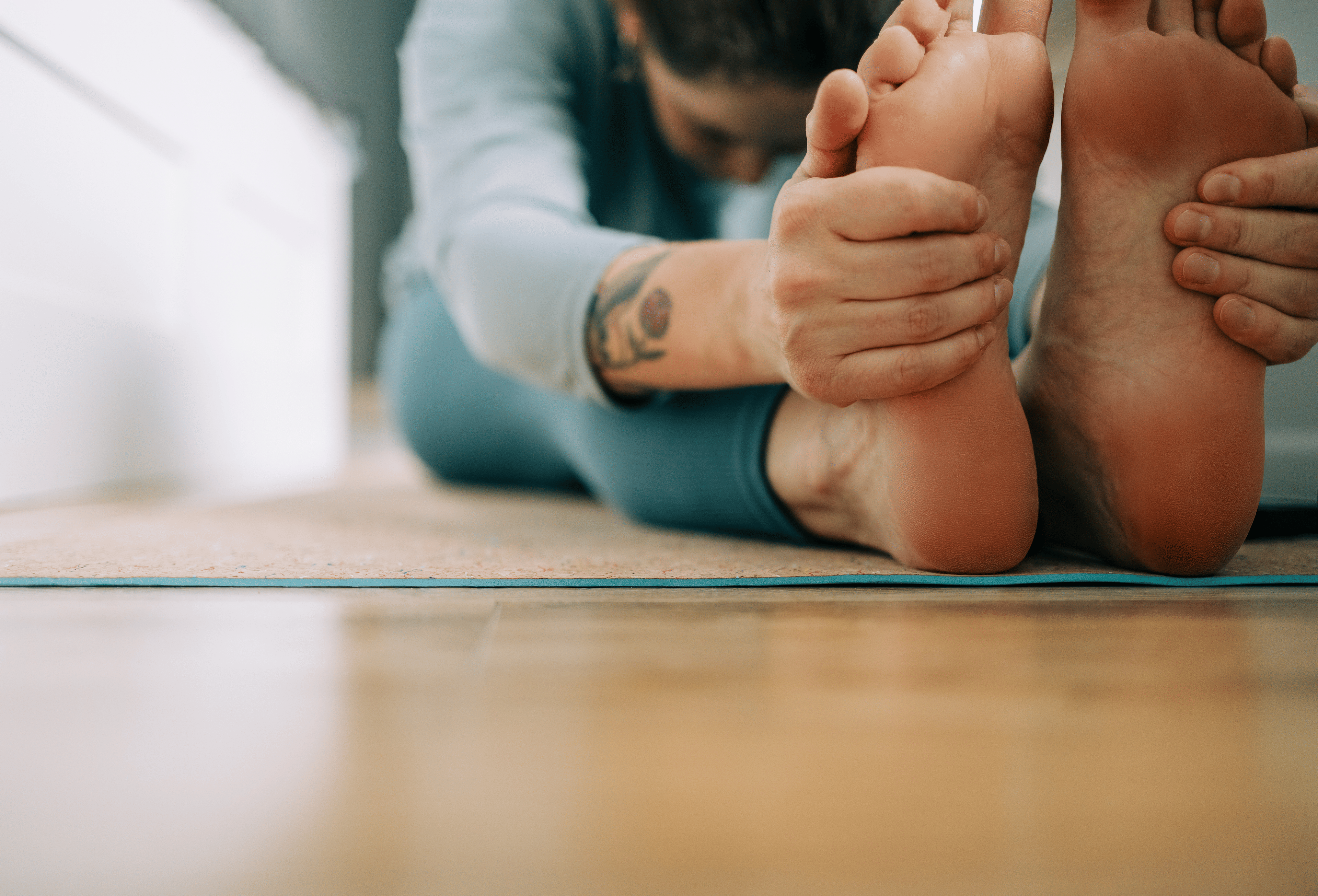 Woman with tattoos doing a Seated Forward Fold while doing yoga for flexibility at home.