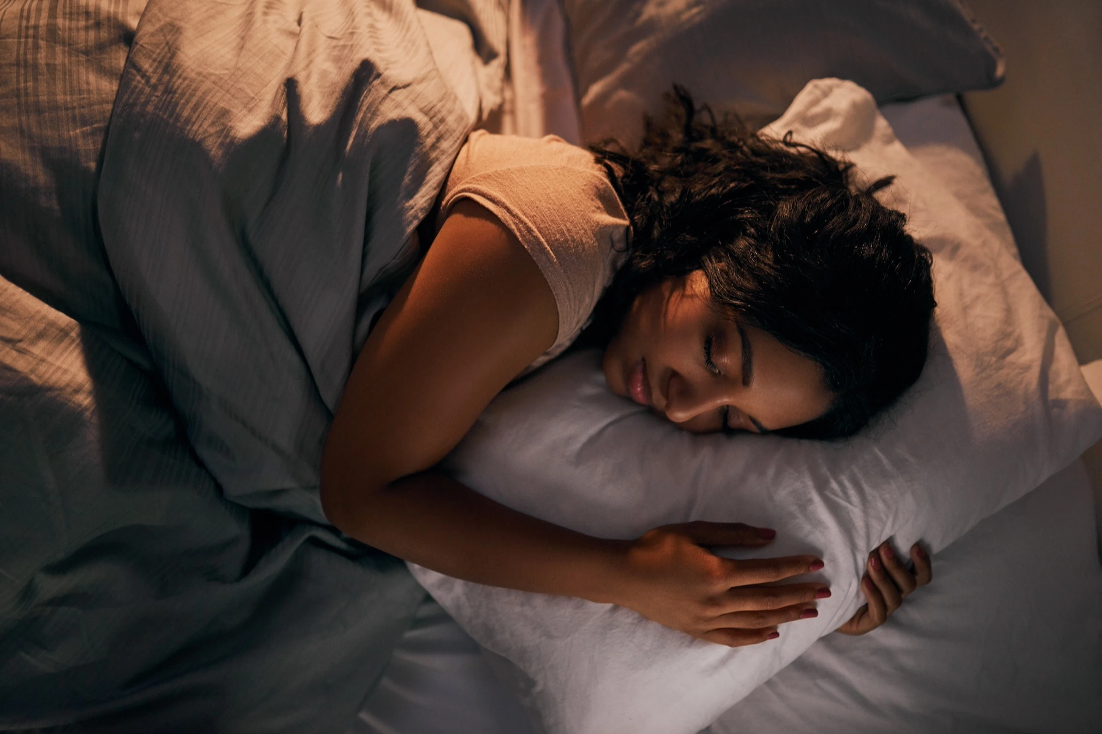 A high-angle shot of a woman sleeping peacefully in a bed, cuddling her pillow.
