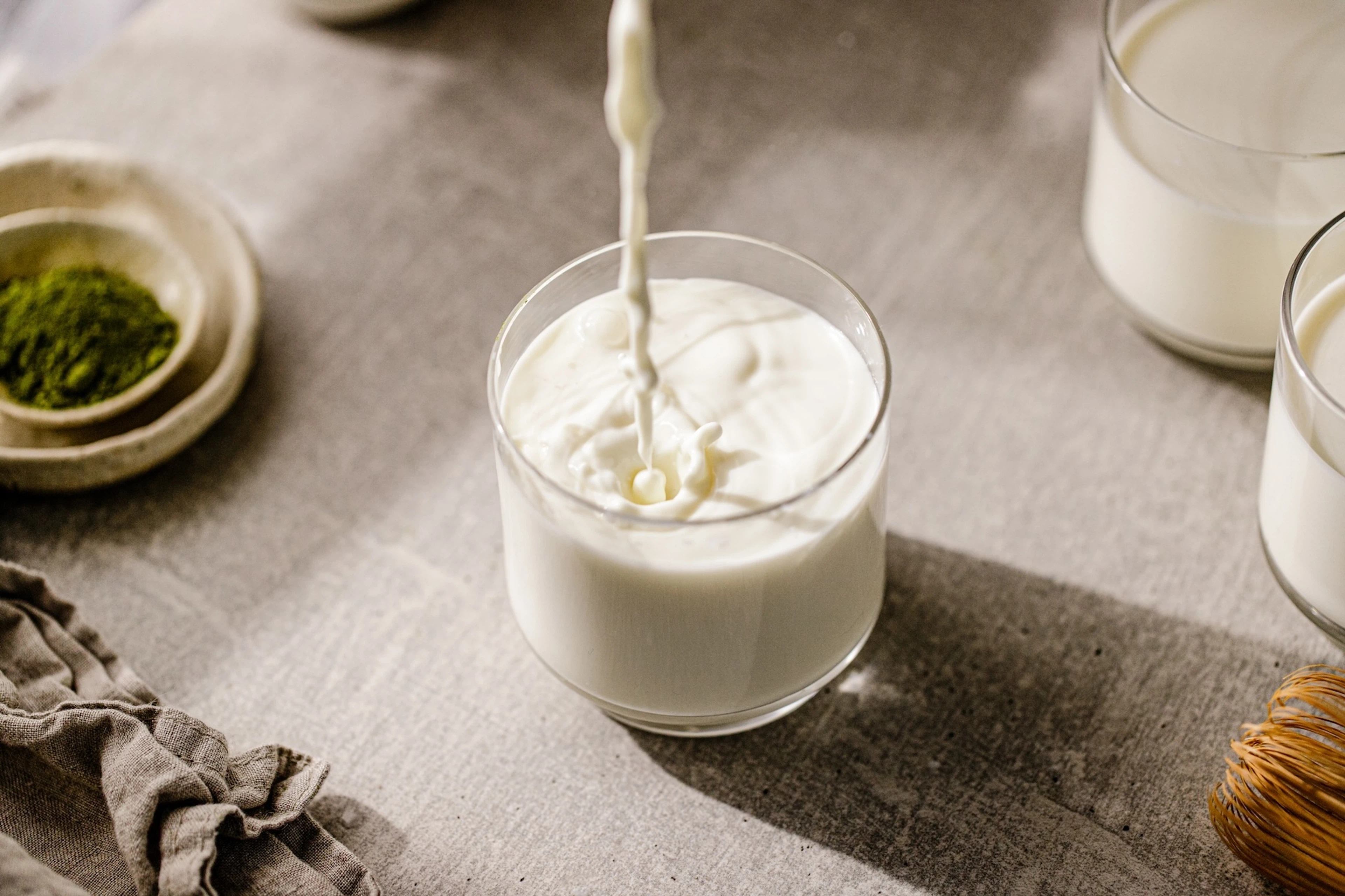 Milk being poured into a glass resting on a table.