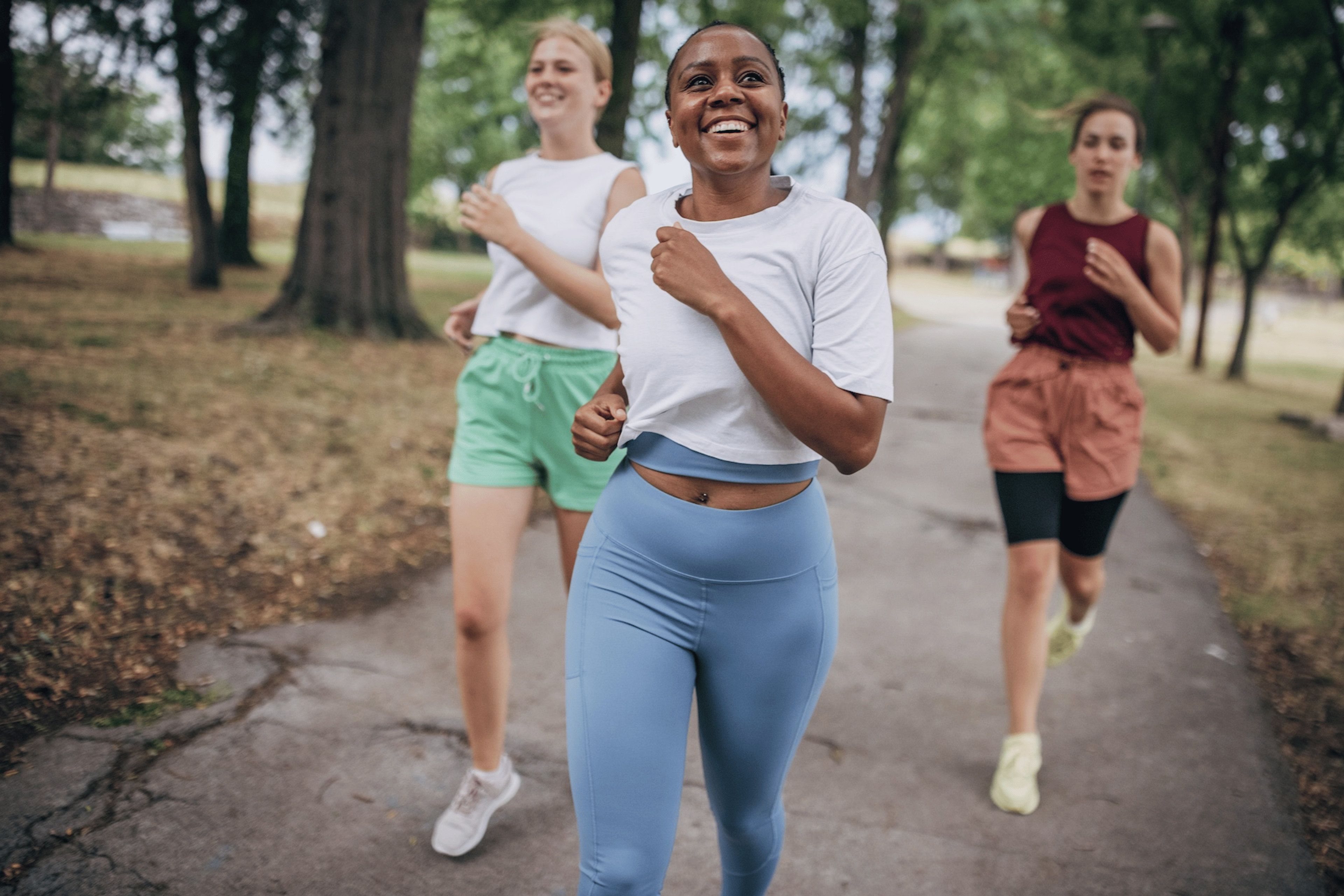 A group of three friends happily running together outside in a park. Learn about intrinsic vs. extrinsic motivation here.