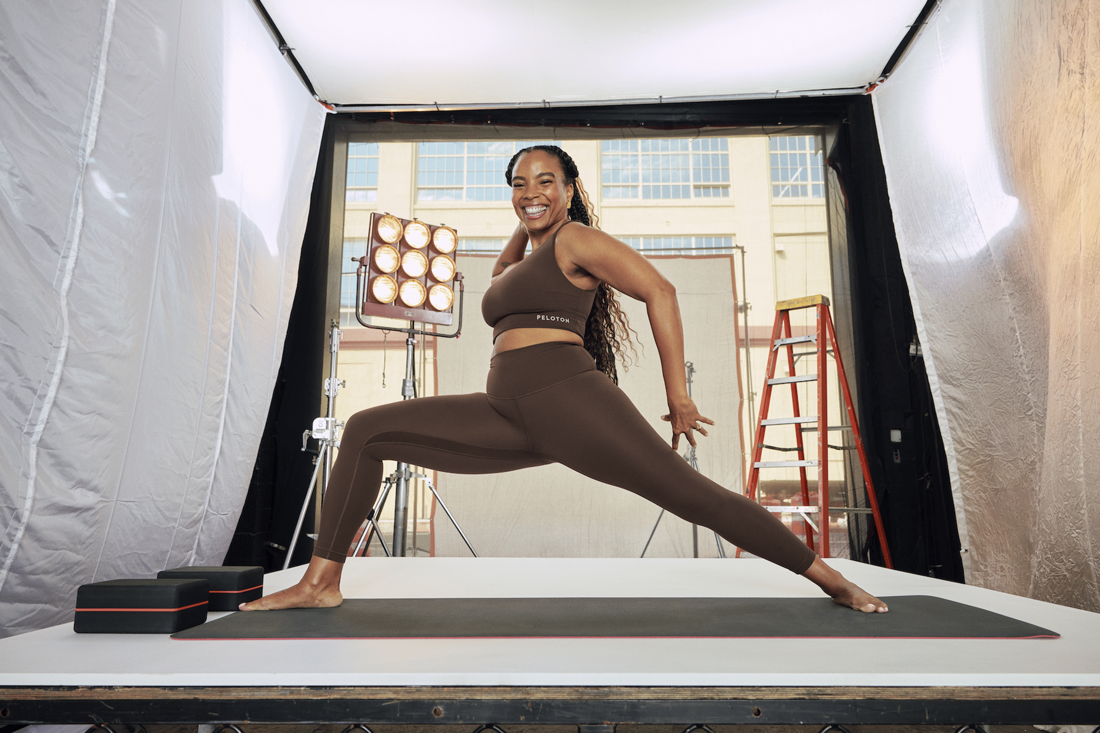 In this image for an article about how gym clothes affect motivation and performance, Peloton instructor Chelsea Jackson Roberts is grinning while doing a forward lunge in a matching brown activewear set.