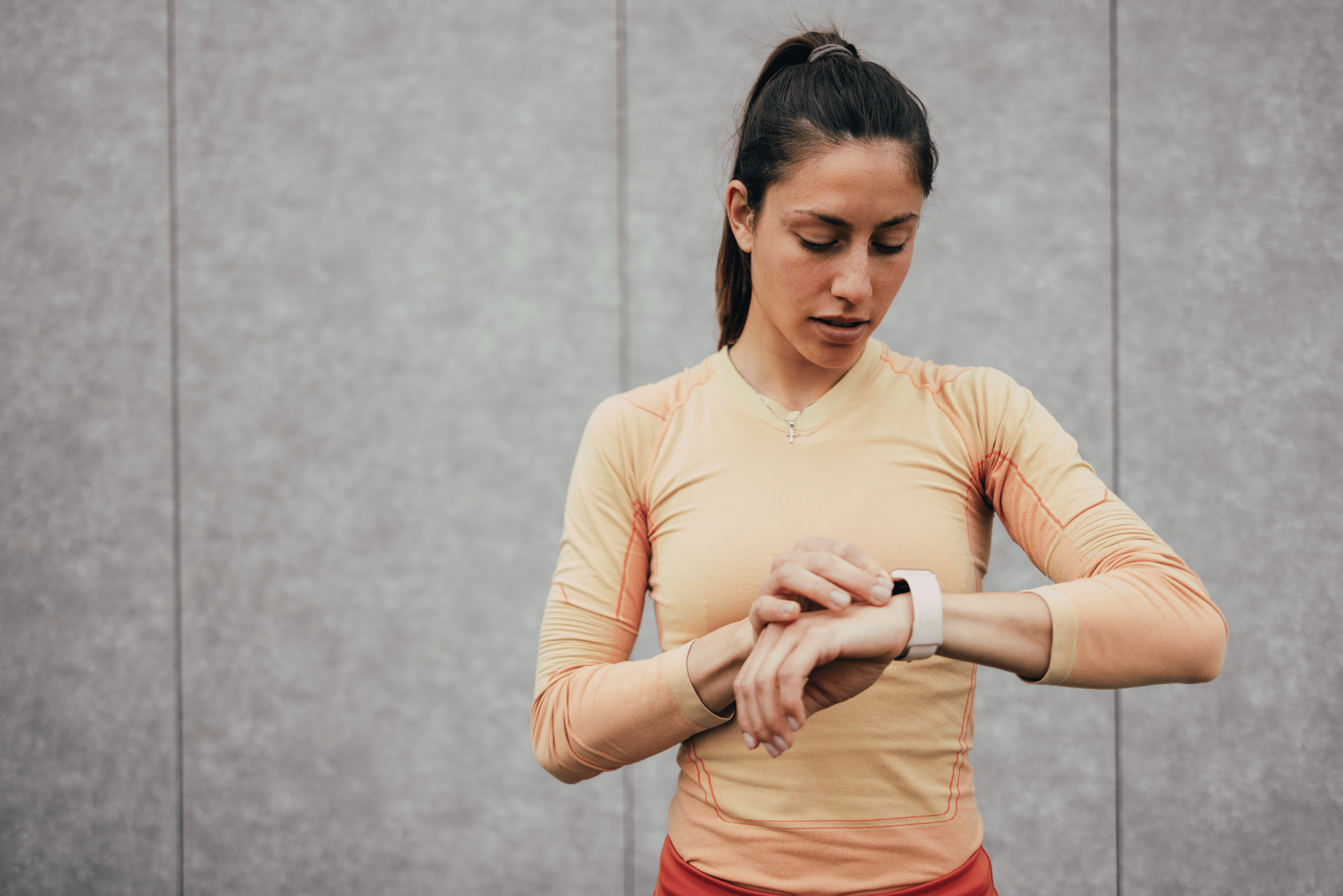 Young woman in fitness gear checking her heart rate zone on a smartwatch during her long run