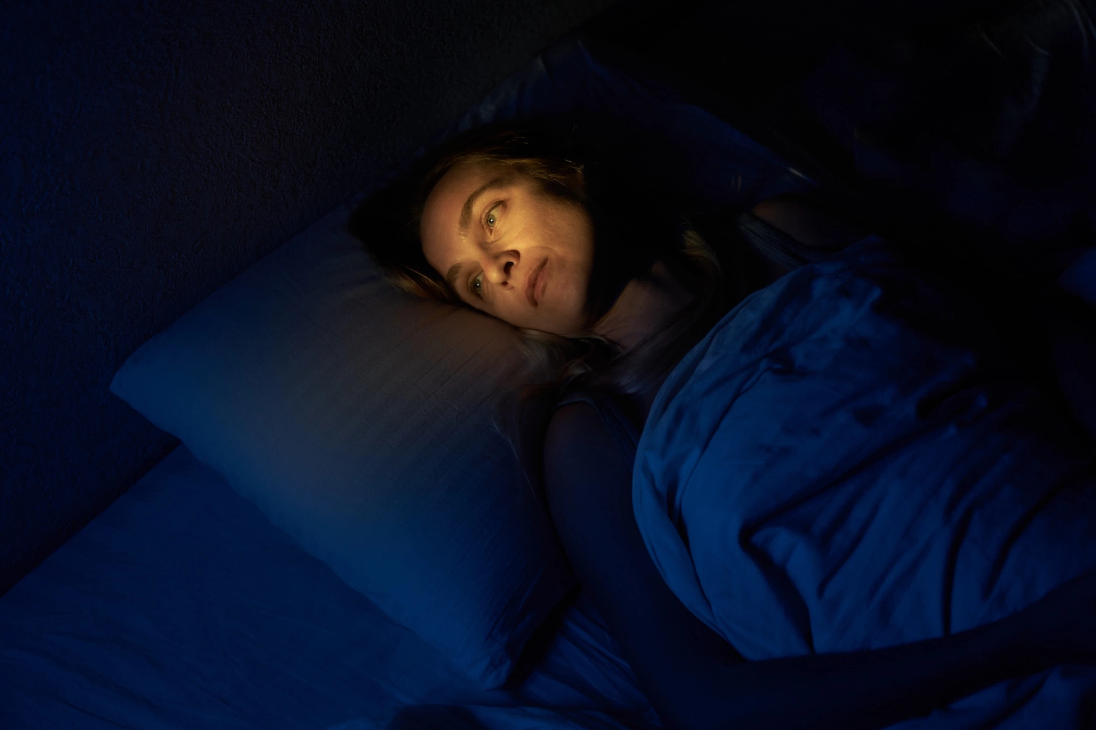 A woman lying awake in bed, experiencing racing thoughts at night.