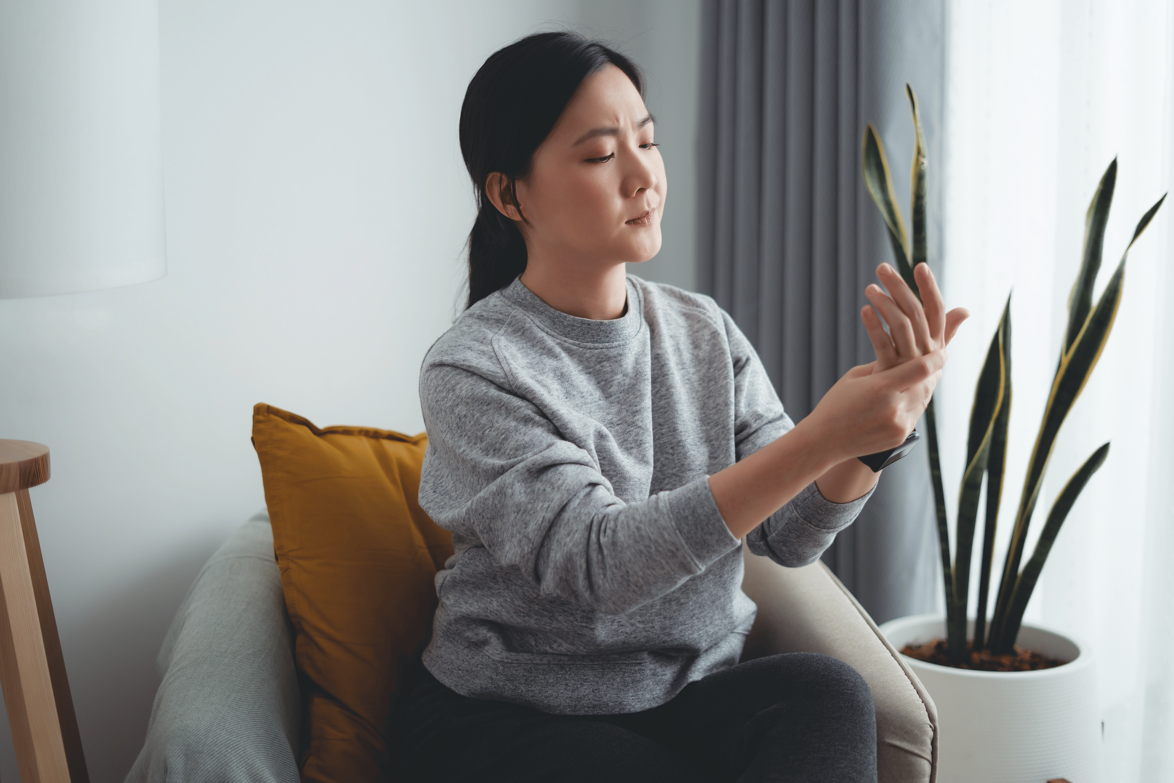 Woman looks at wrist and hand while sitting in a chair 