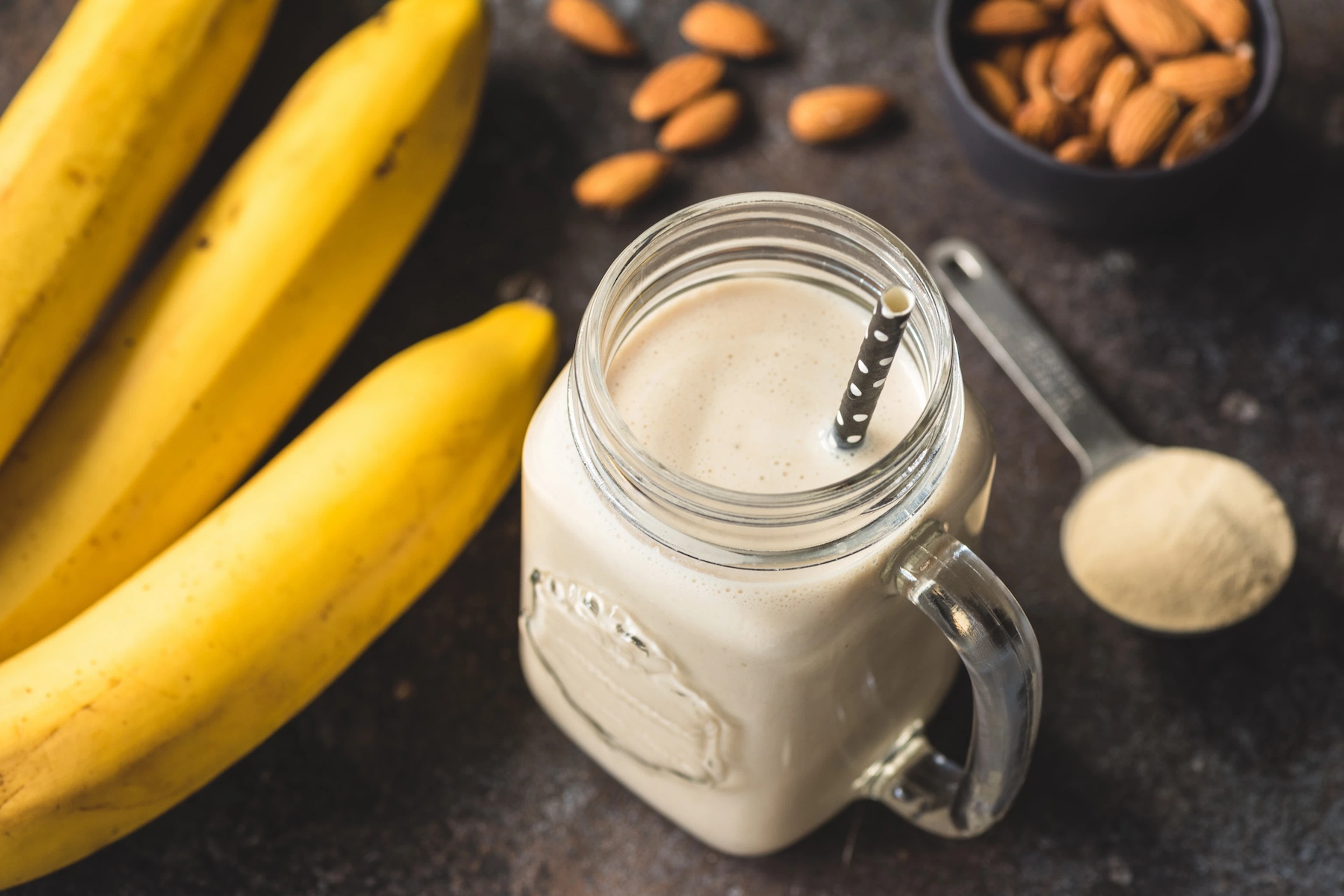 A banana smoothie in a glass mason jar with a handle and straw.
