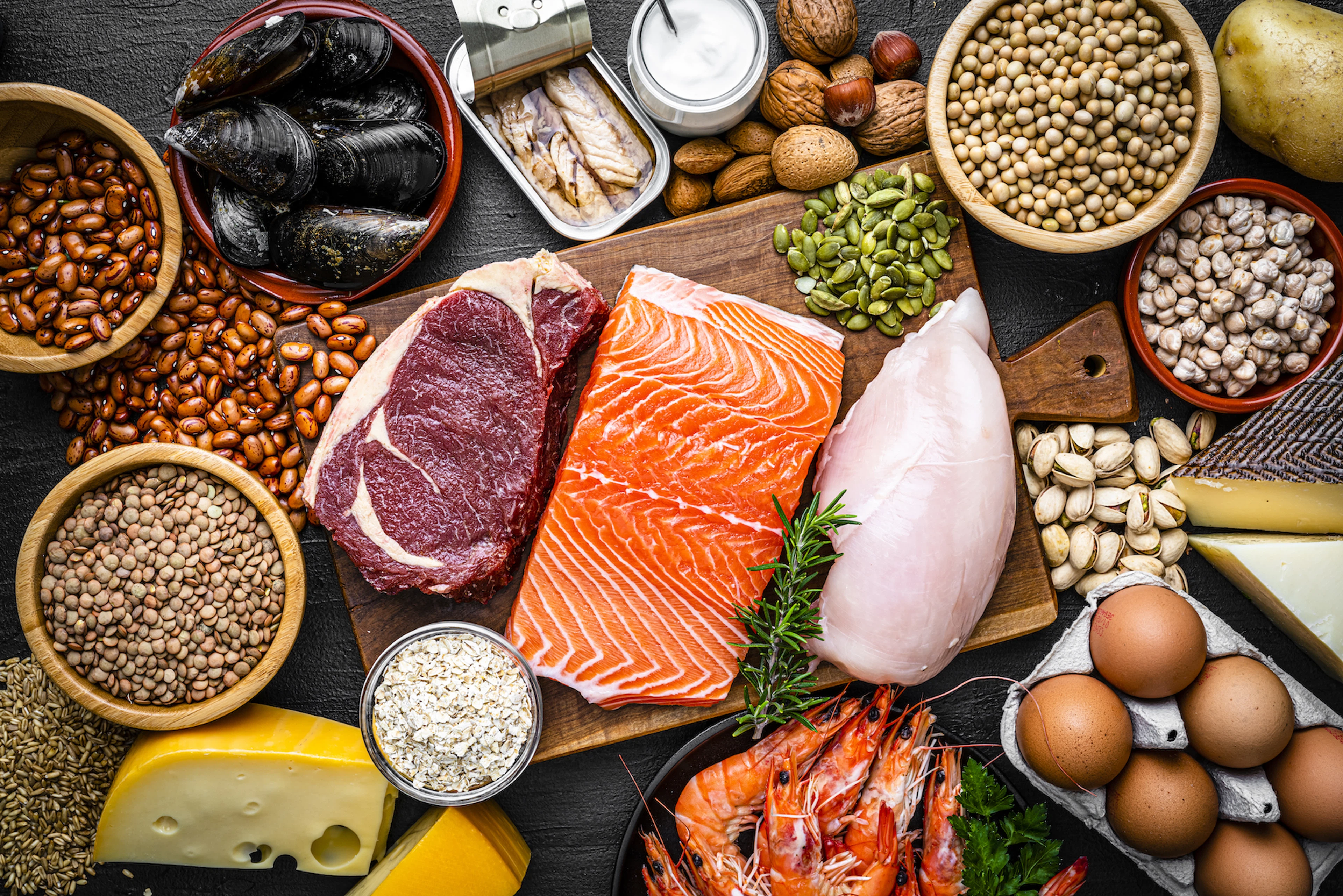 A flay-lay photograph of protein-rich foods like fish, eggs, and legumes.