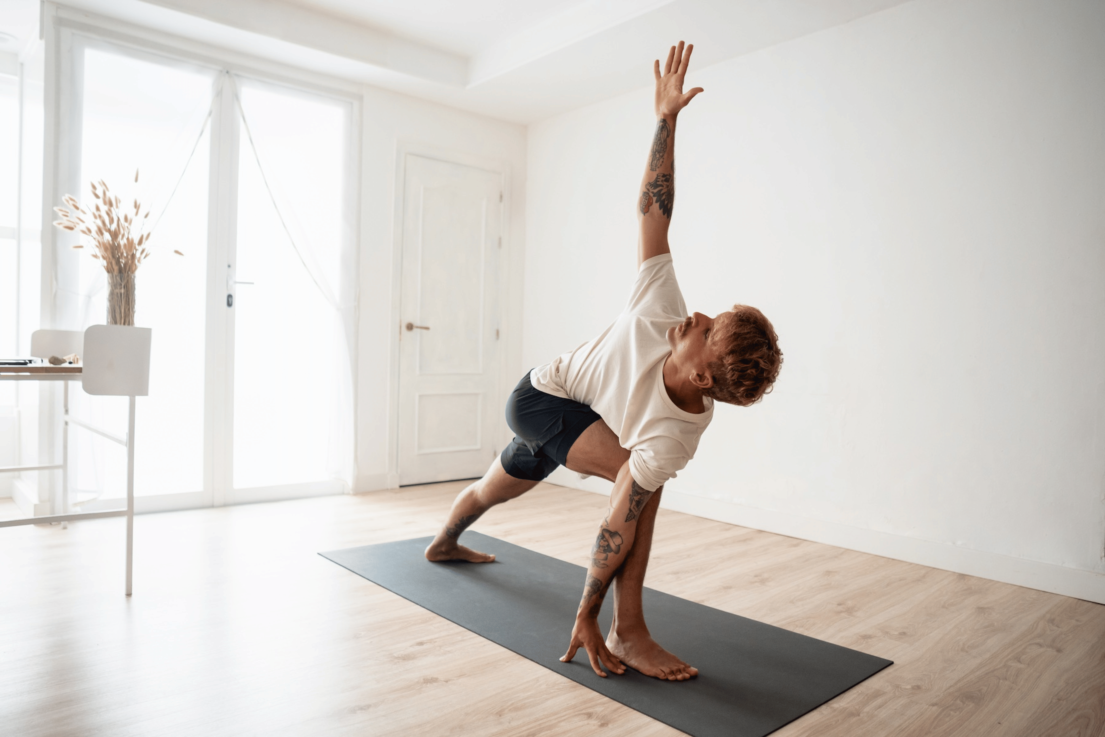 A man doing yoga before or after a workout. He's doing Triangle Pose on a yoga mat at home.