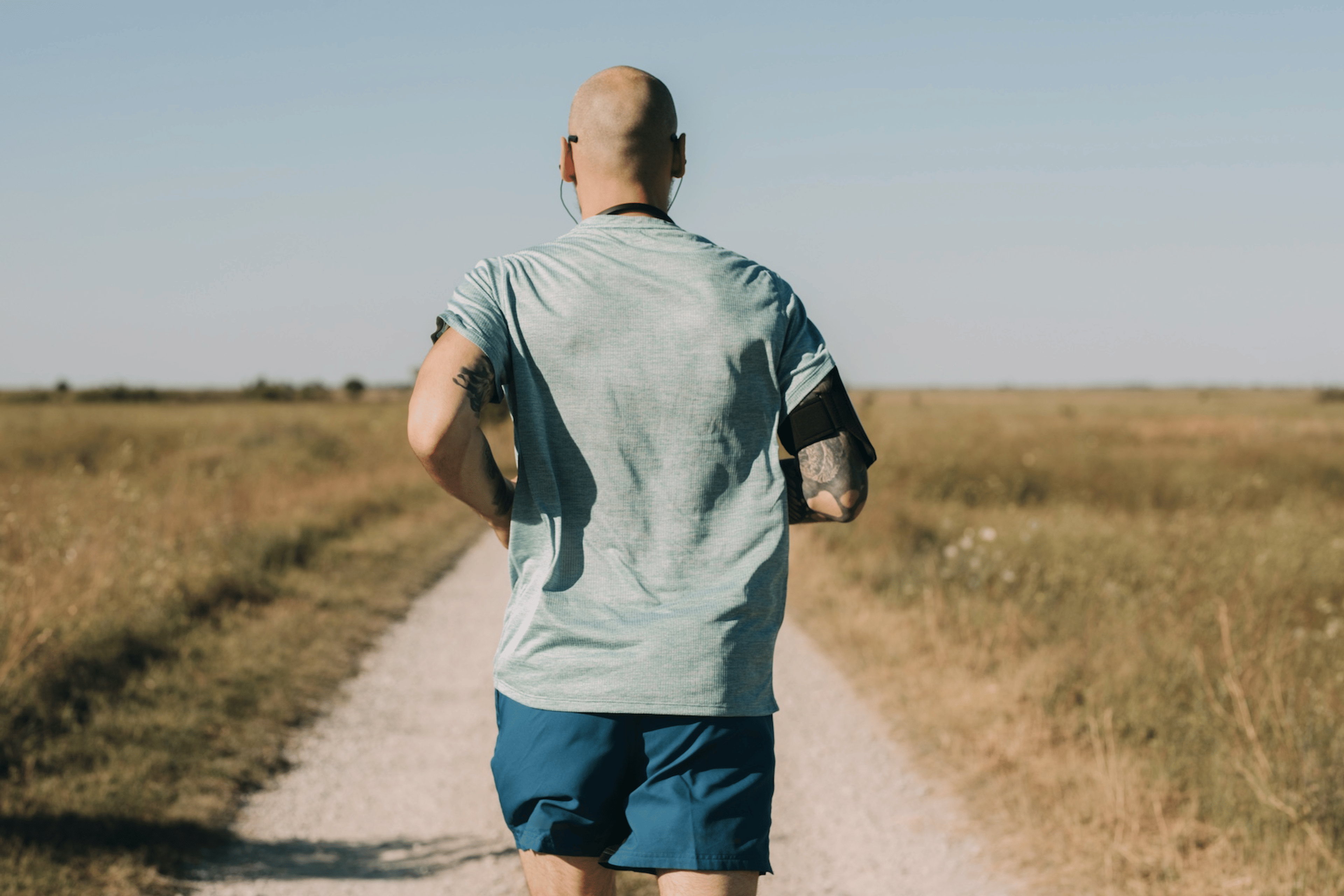 Back view of a man going for a run outside surrounded by fields.