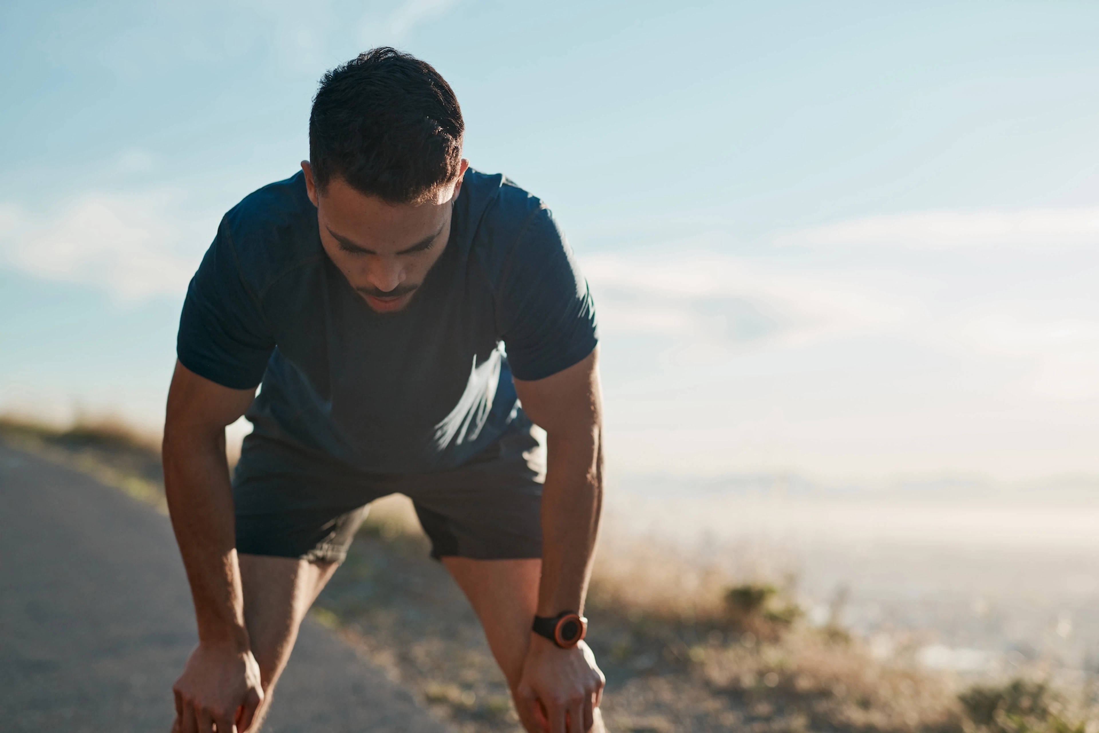 An athlete with his head down, resting his hands on his knees. He is experiencing signs of overtraining like fatigue.
