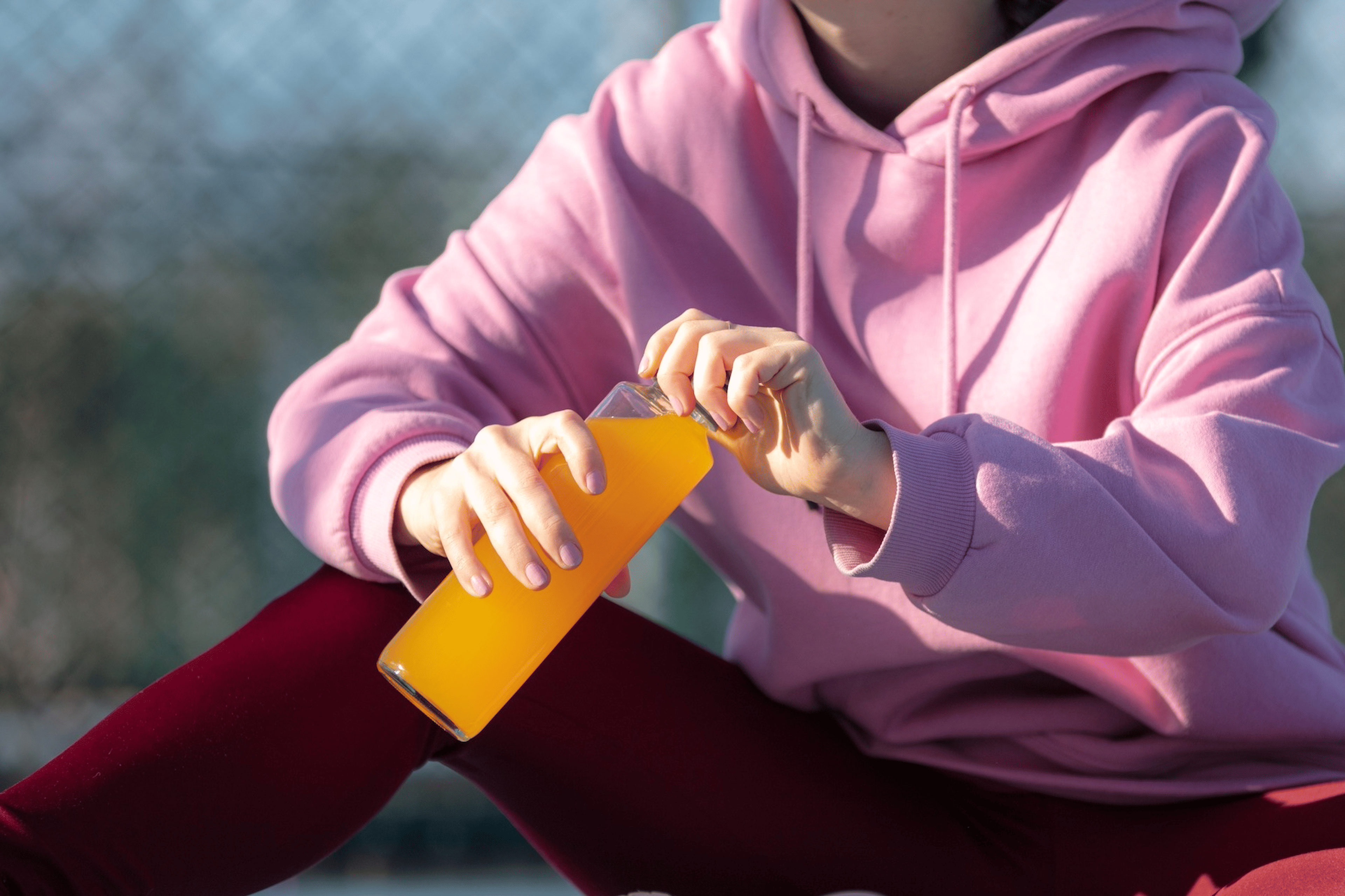 A woman drinking an orange electrolyte drink before or after a workout.