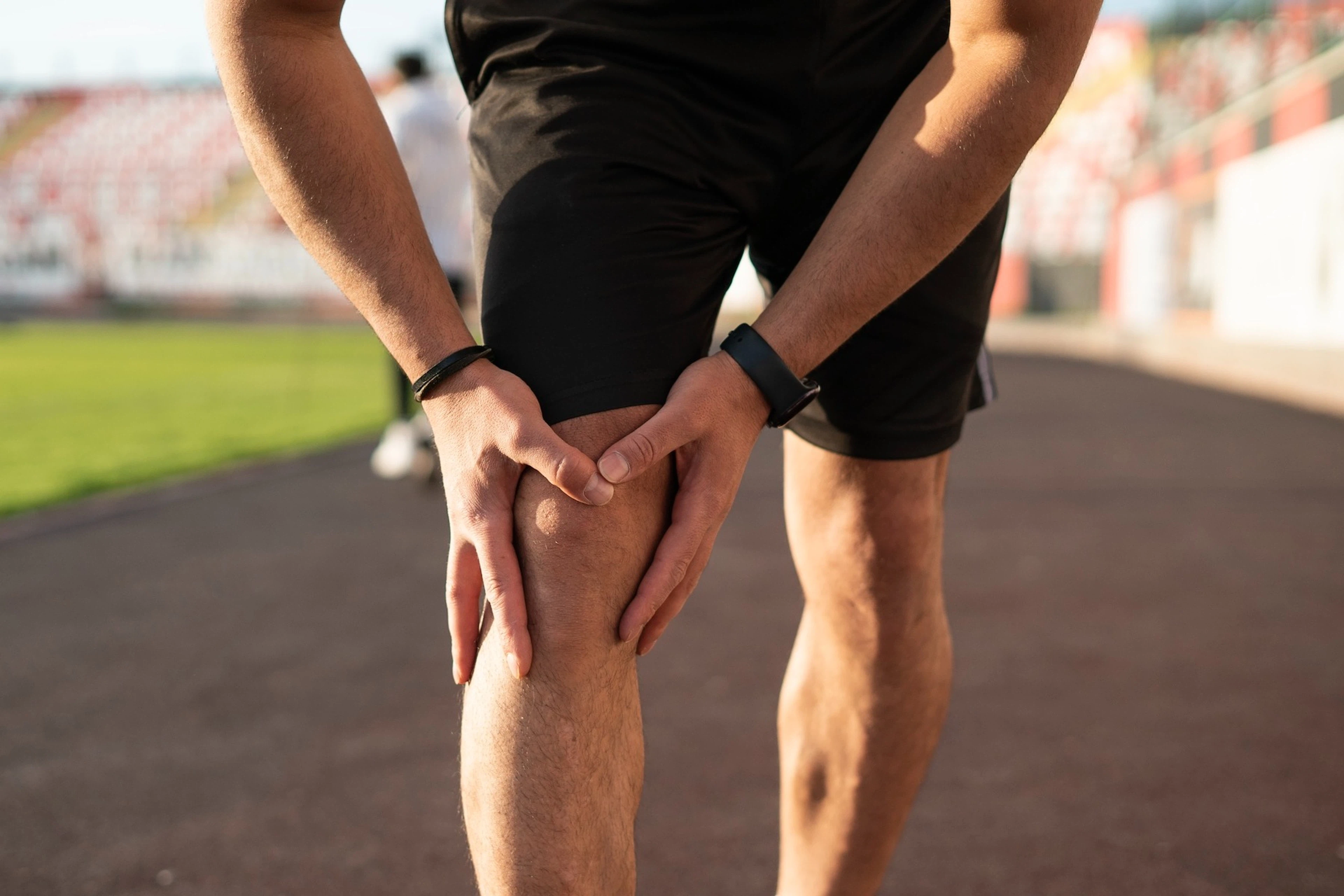 A man experiencing runner's knee. It's a zoomed-in photo of him holding onto the front of his right knee after an outdoor jog.