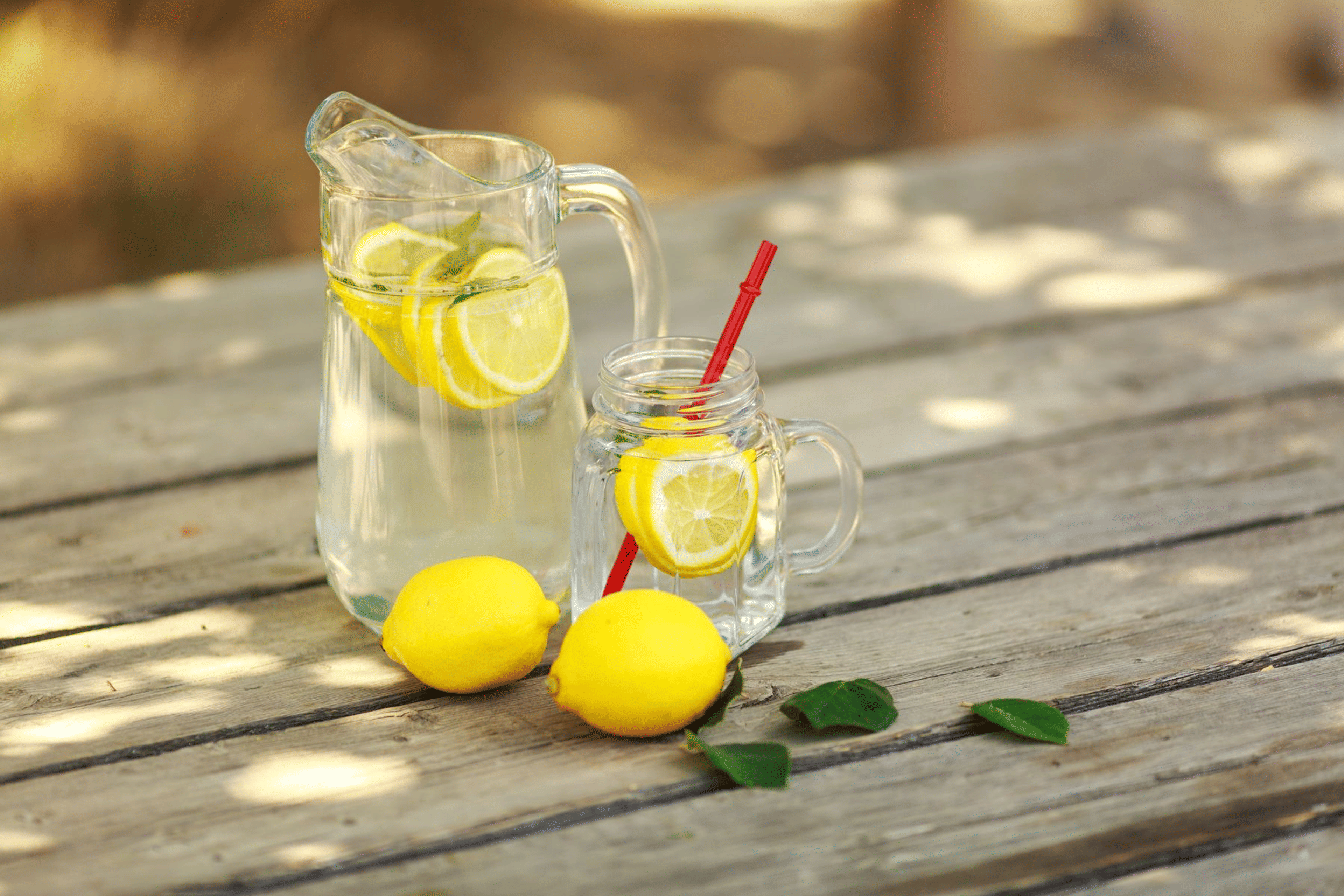 A pitcher and a glass of lemon water on a wooden picnic table