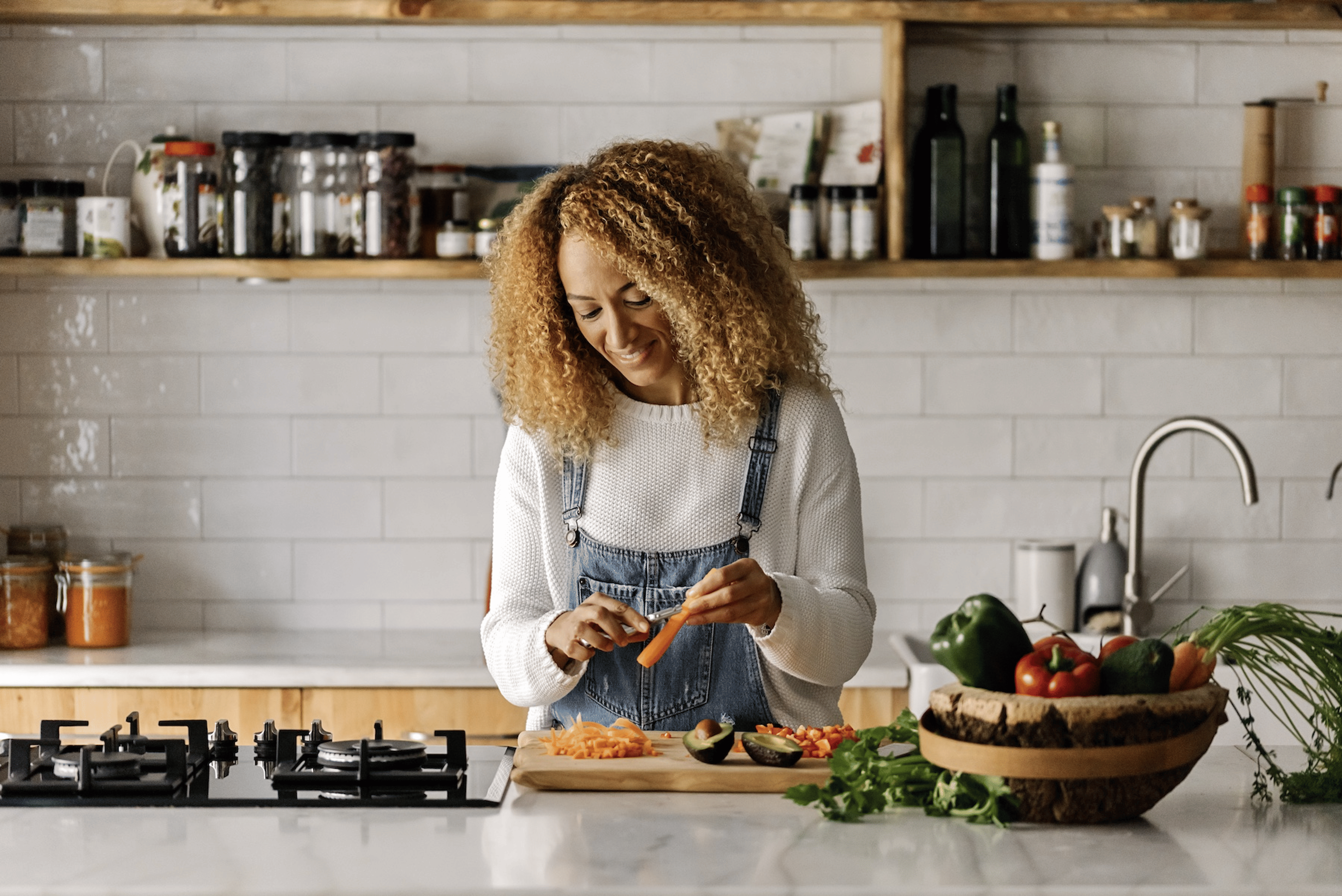 A woman smiling and peeling a carrot in her kitchen to eat more vegetables.