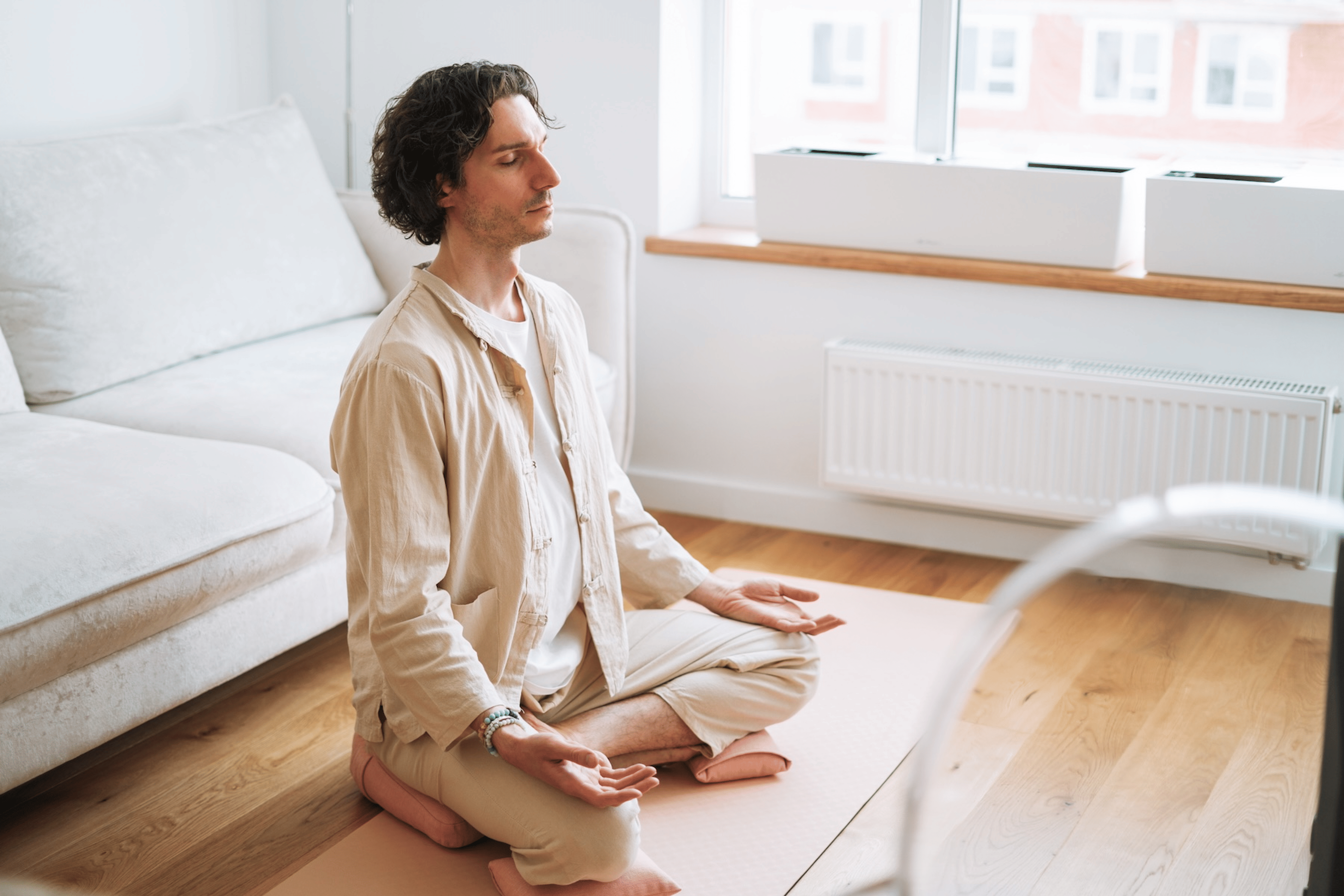 A man in a seated meditation position. He's resting on a pillow for support with his hands on his knees, his back straight, and his eyes closed.