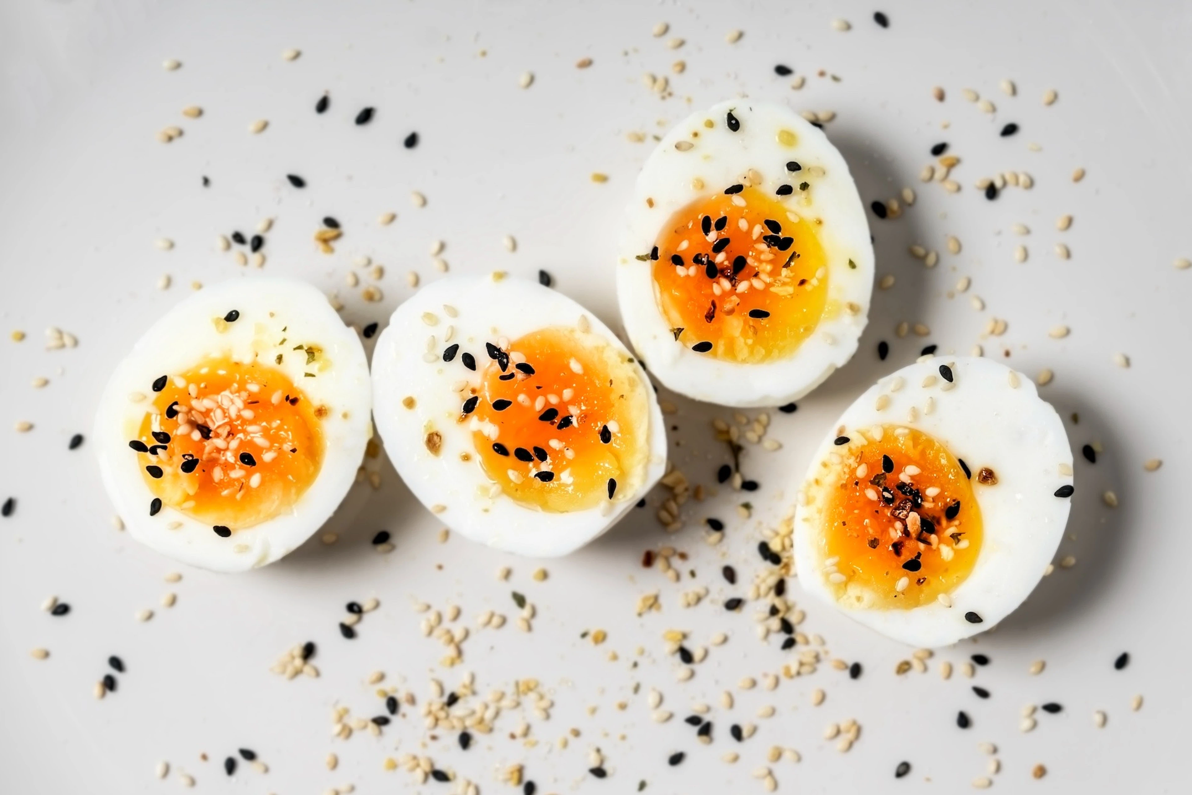 Four halved hard-boiled eggs with everything bagel seasoning resting on a white background.
