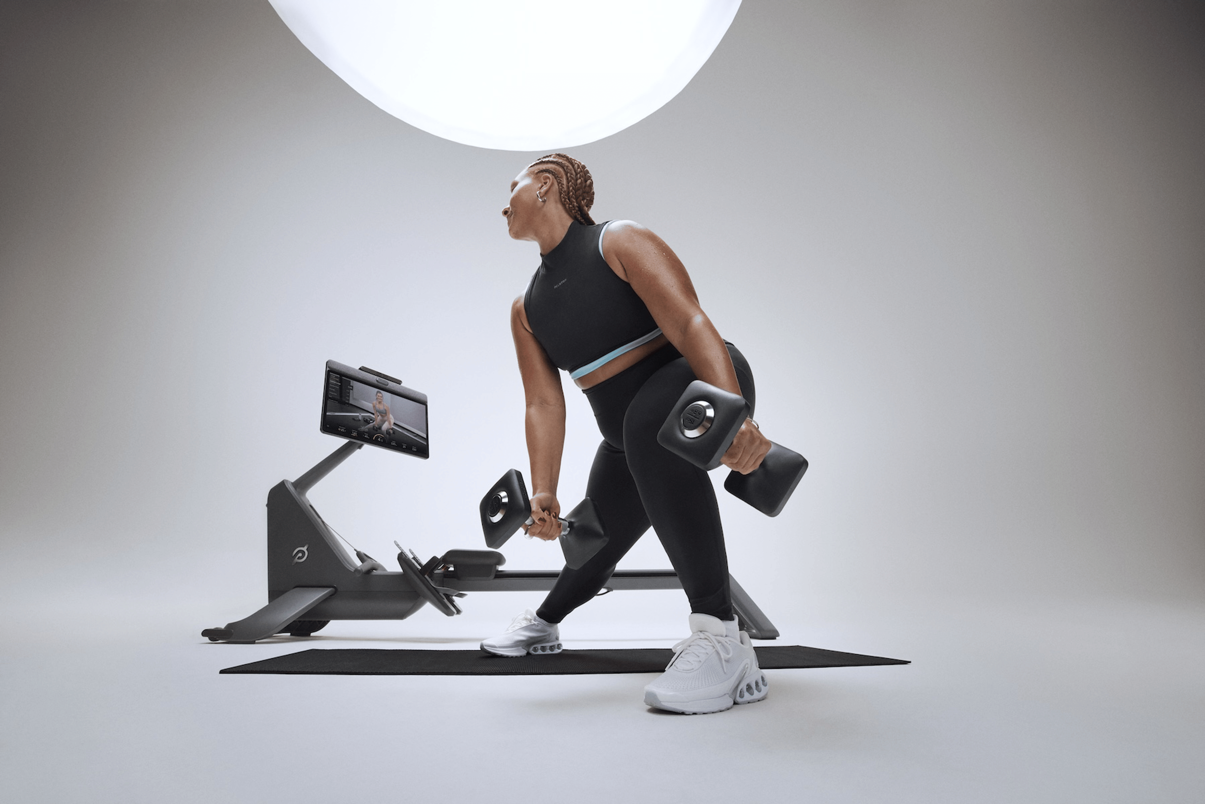 A woman doing a Peloton strength workout with dumbbells on the Peloton Cross Training Series Row+ Powered by Peloton IQ.