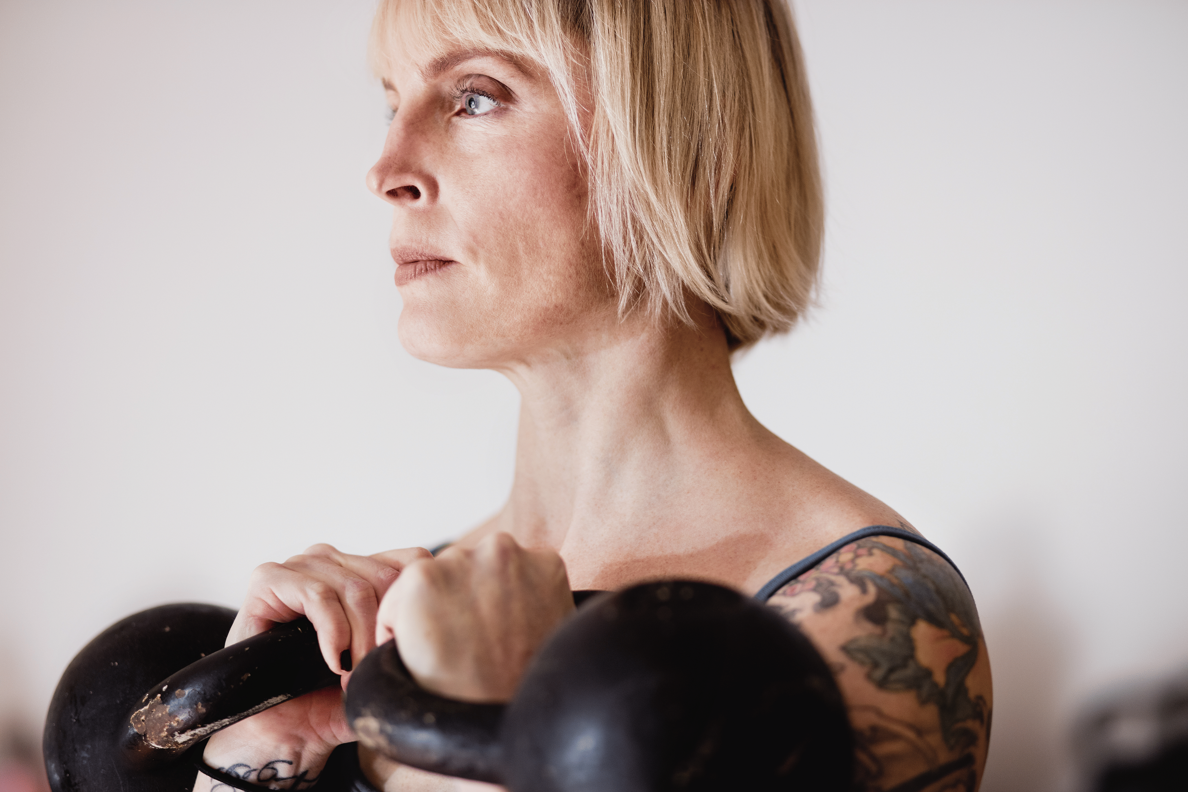 Woman with tattoos holding two kettlebells racked at shoulder height while doing kettlebell shoulder exercises