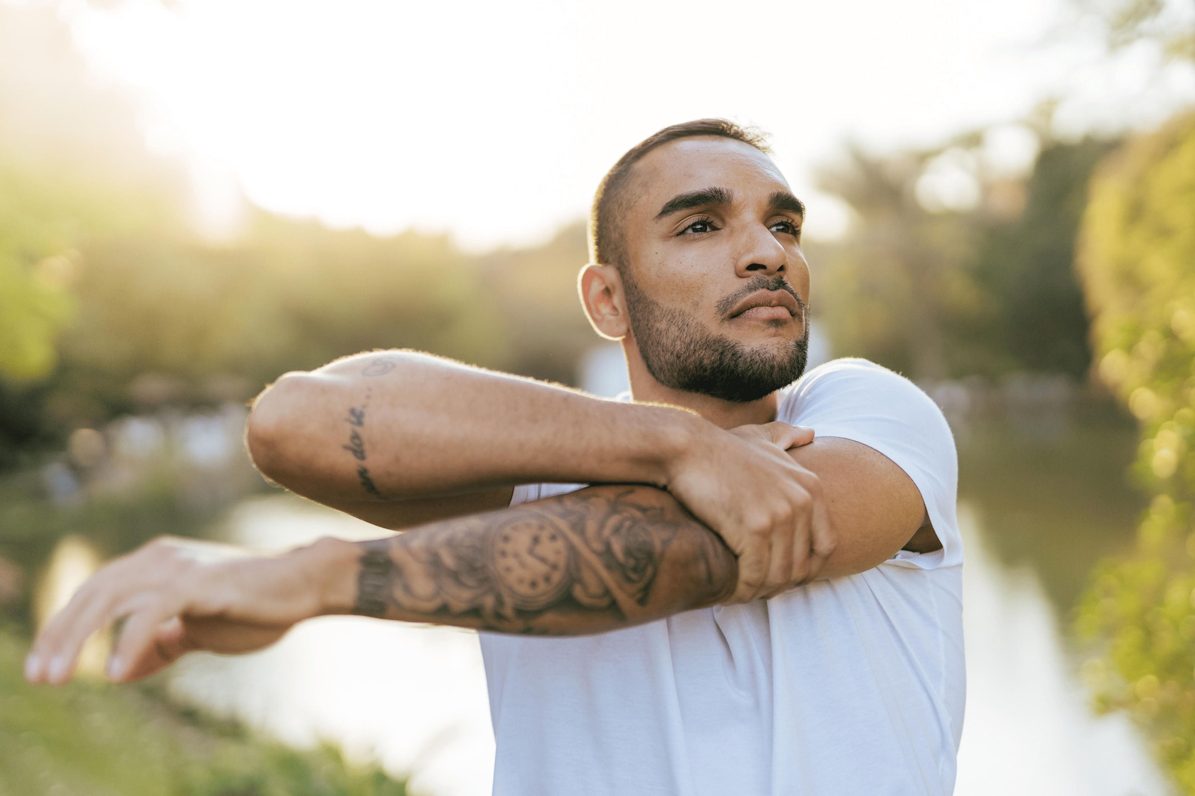 Wellness Trends: A young athlete stretching his arms in a park at sunset.