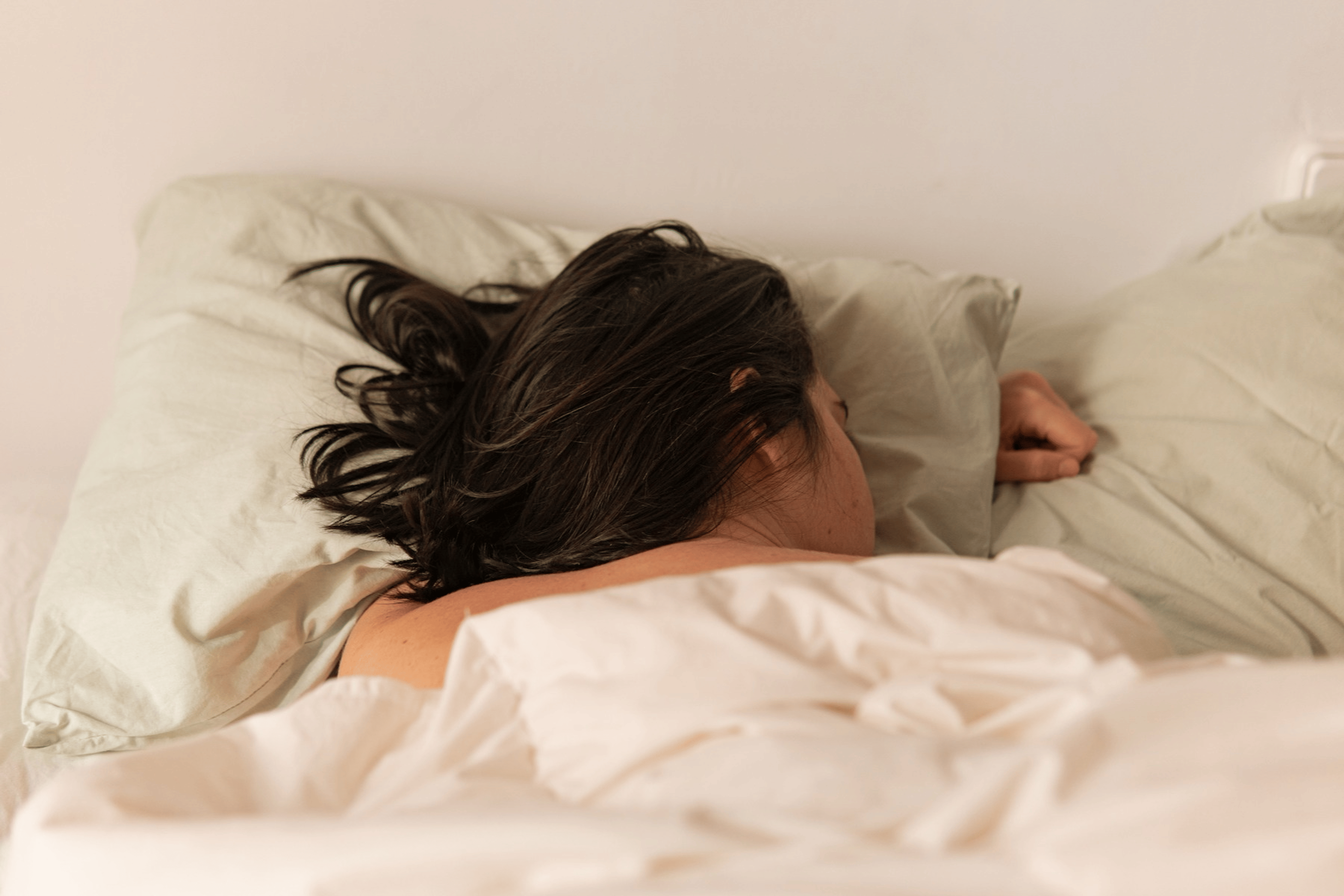 A woman sleeping in bed on her belly. Learn whether or not it is bad to sleep with wet hair in this article.